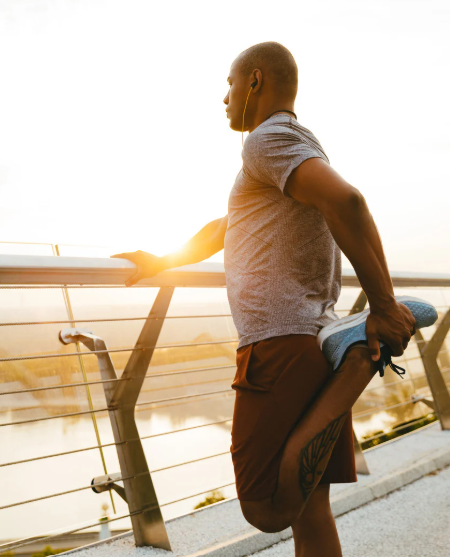 Man stretching his leg on bridge overlooking water in the early morning.