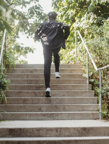 A person running up outdoor concrete stairs surrounded by greenery on a sunny day.