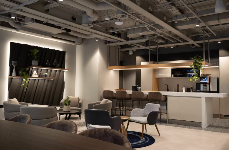 Modern lounge with seating area, bar counter, and open kitchen, decorated with plants and contemporary furniture.