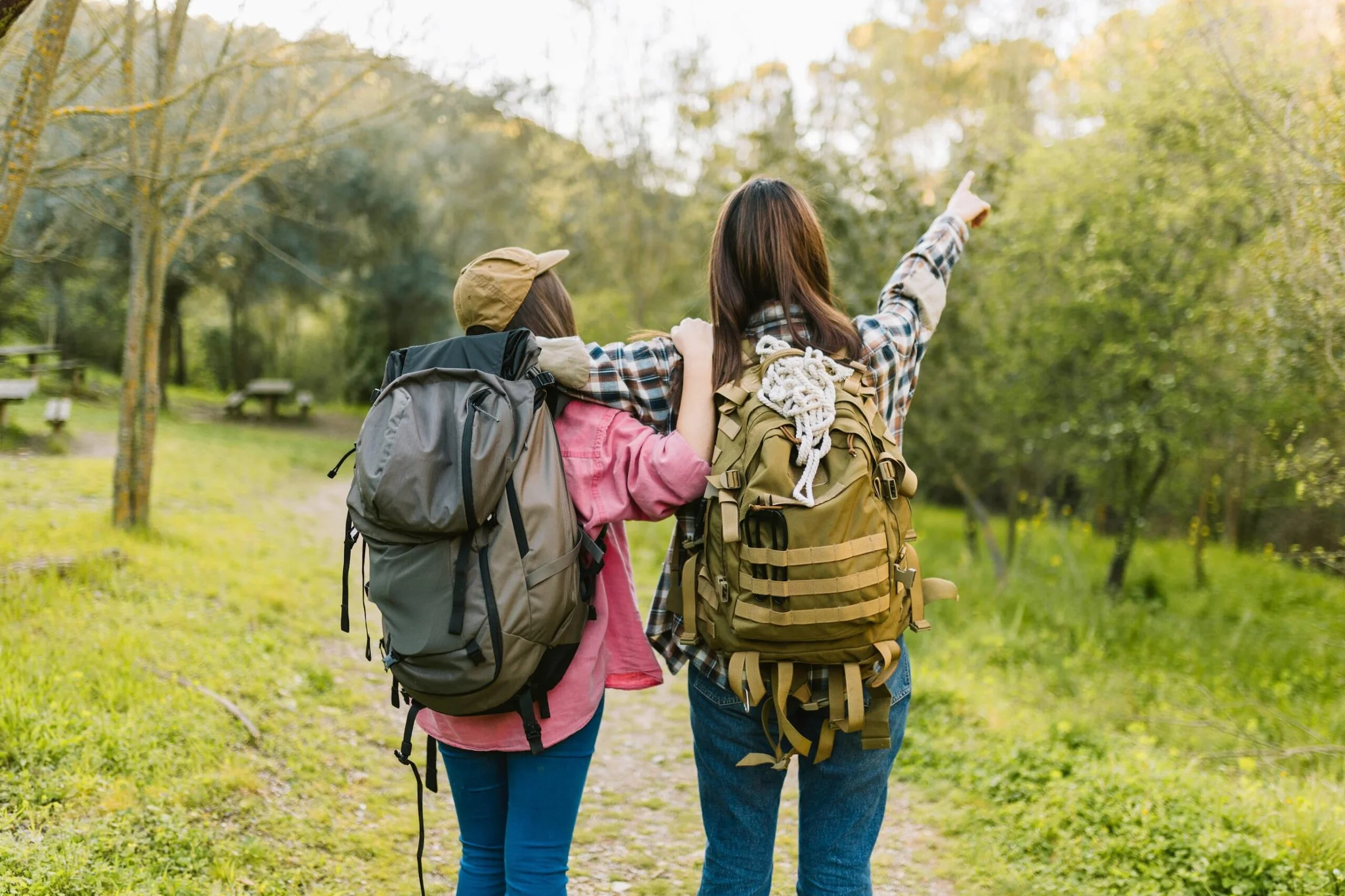 Deux femmes portant des sacs à dos font une randonnée dans une forêt verte, l'une d'elles pointe du doigt vers l'horizon.
