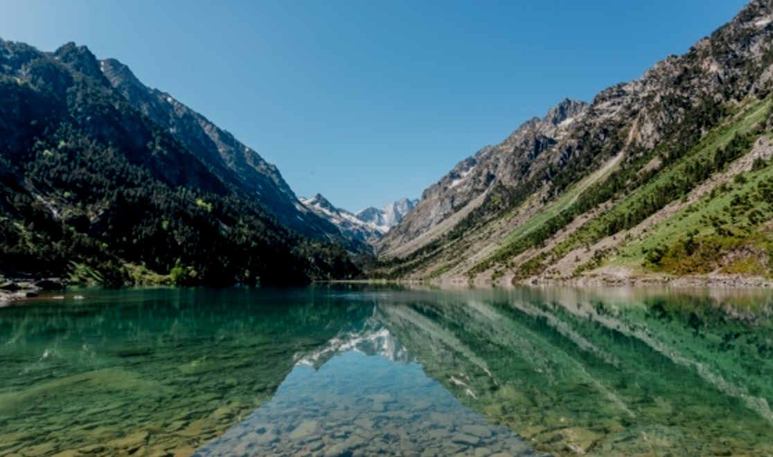 Un lac au milieu de montagnes verdoyantes sous un ciel bleu clair.
