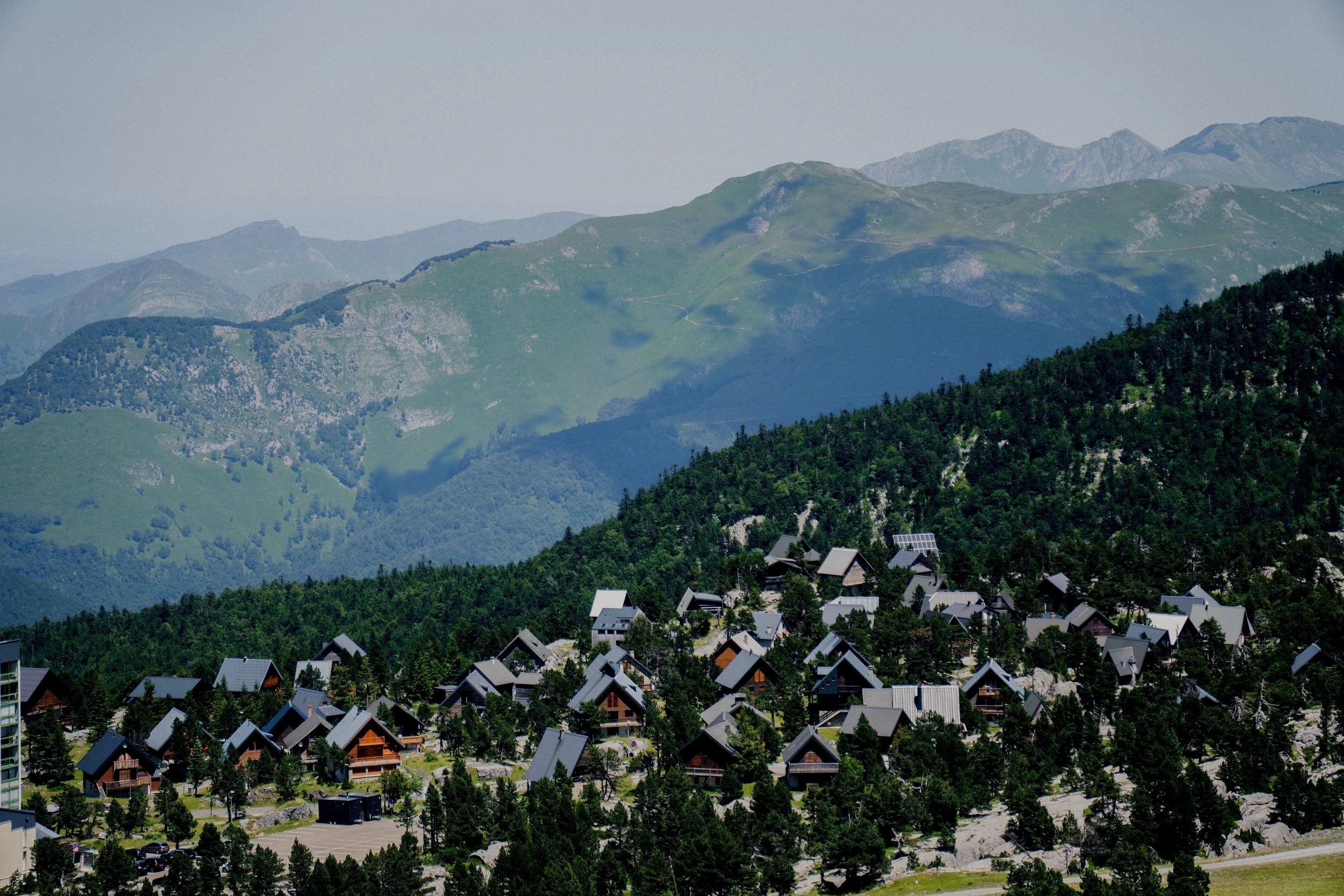 Un village de montagnes avec des maisons et des toits en pente, entouré de collines verdoyantes et de montagnes au loin.