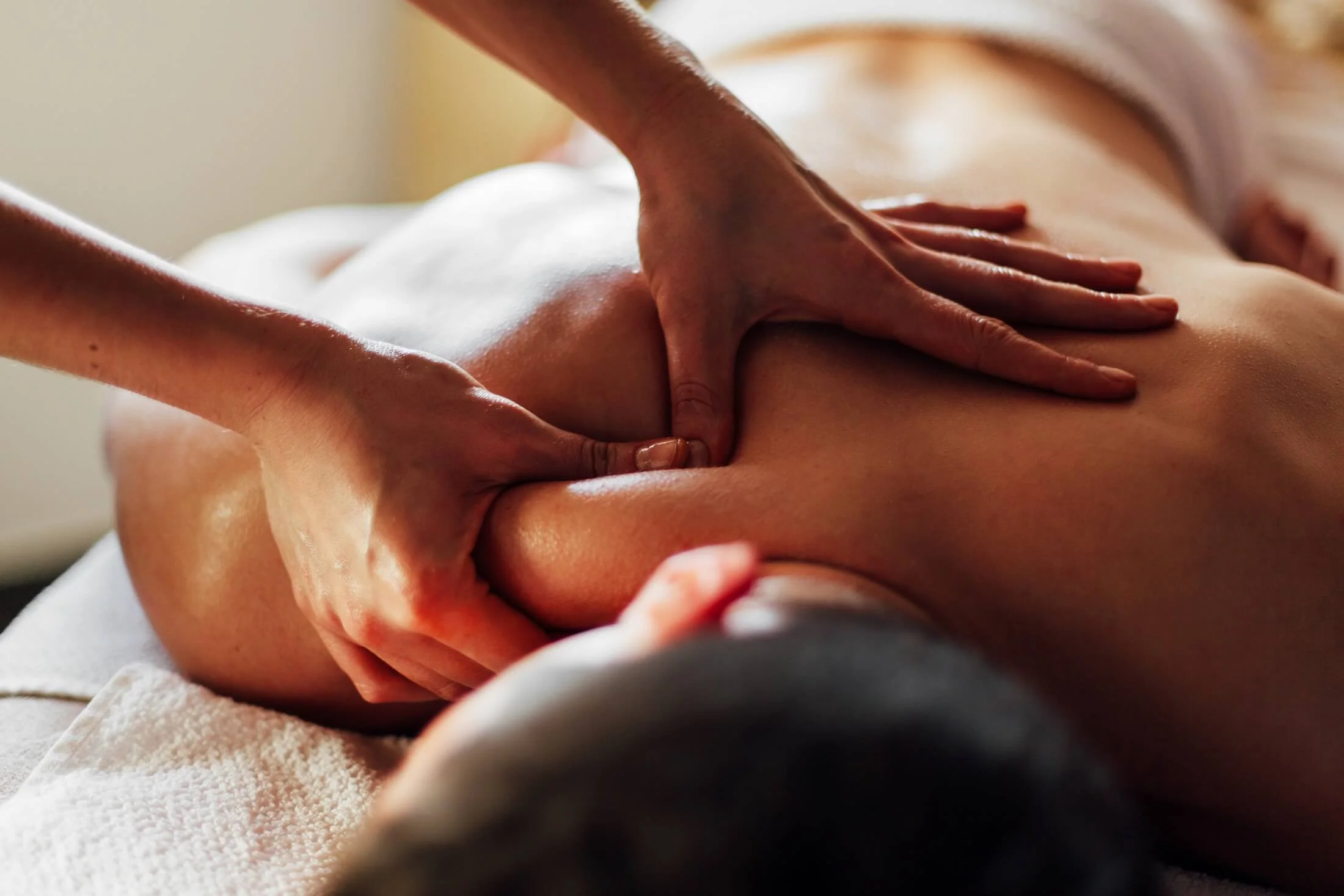 Une personne reçoit un massage sur le dos, allongée sur une table, dans un environnement calme et chaleureux.