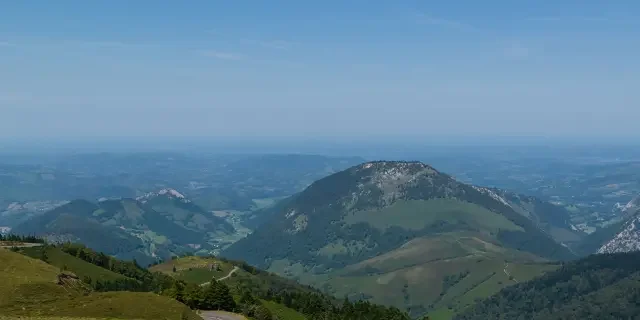 Vue panoramique de montagnes verdoyantes et de vallées sous un ciel clair.