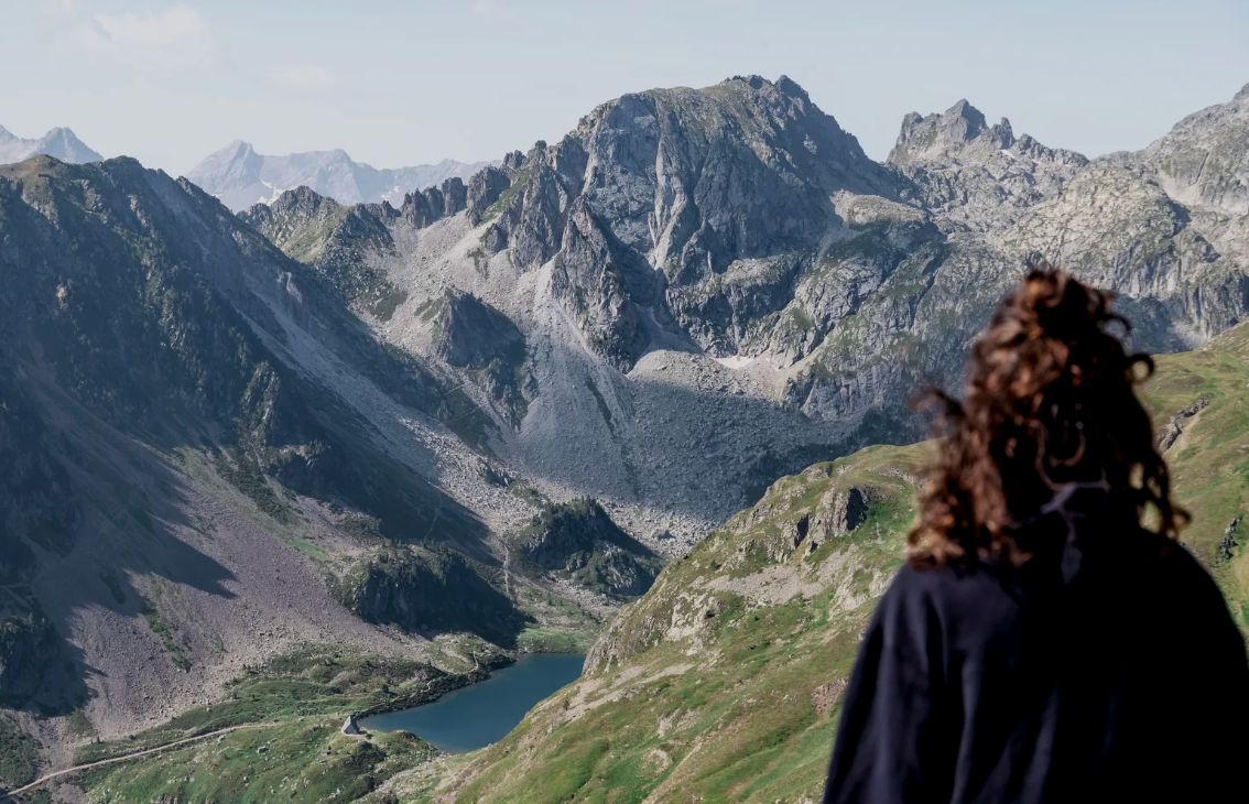 Une femme regarde un paysage de montagnes alpines avec un lac au fond.