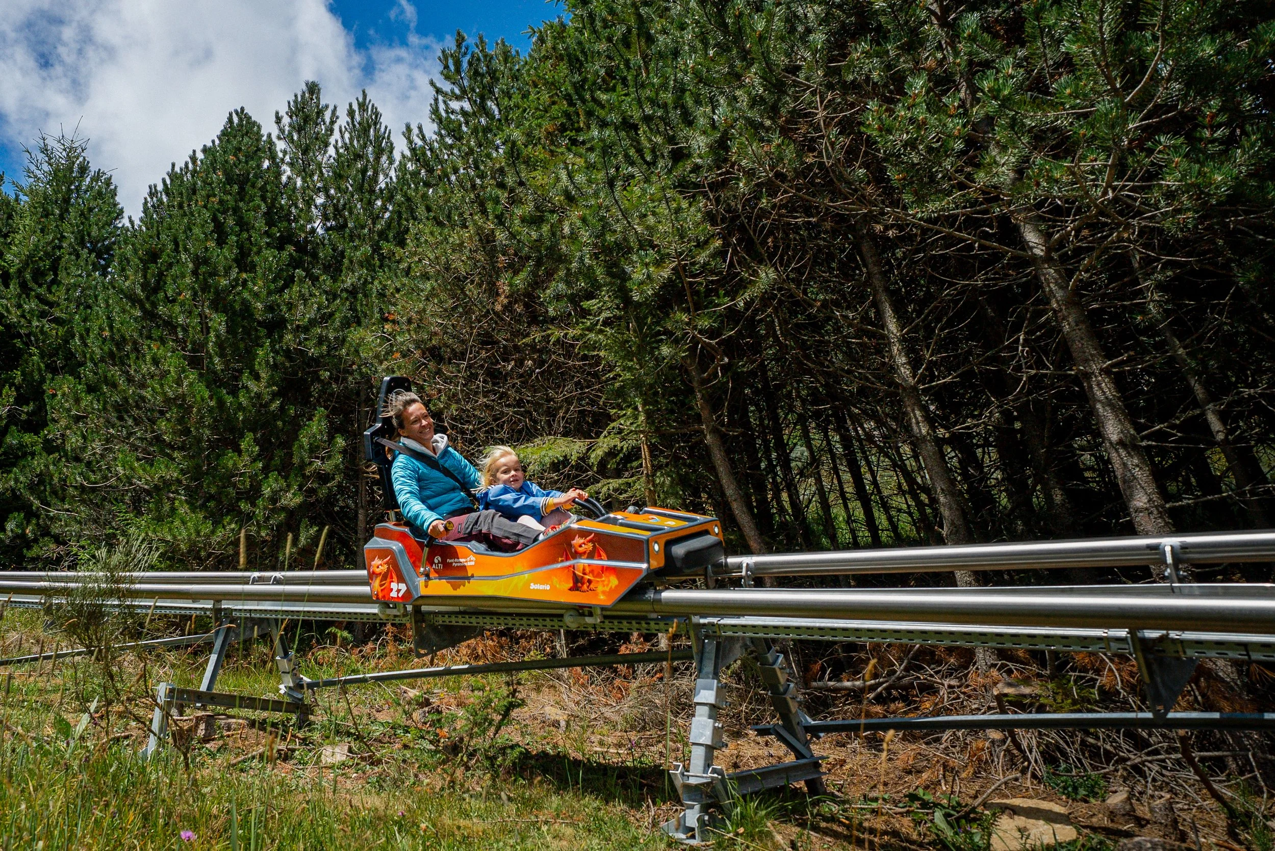 Deux personnes, une femme et un enfant, dans un véhicule d'attraction de type roller coaster dans une forêt.