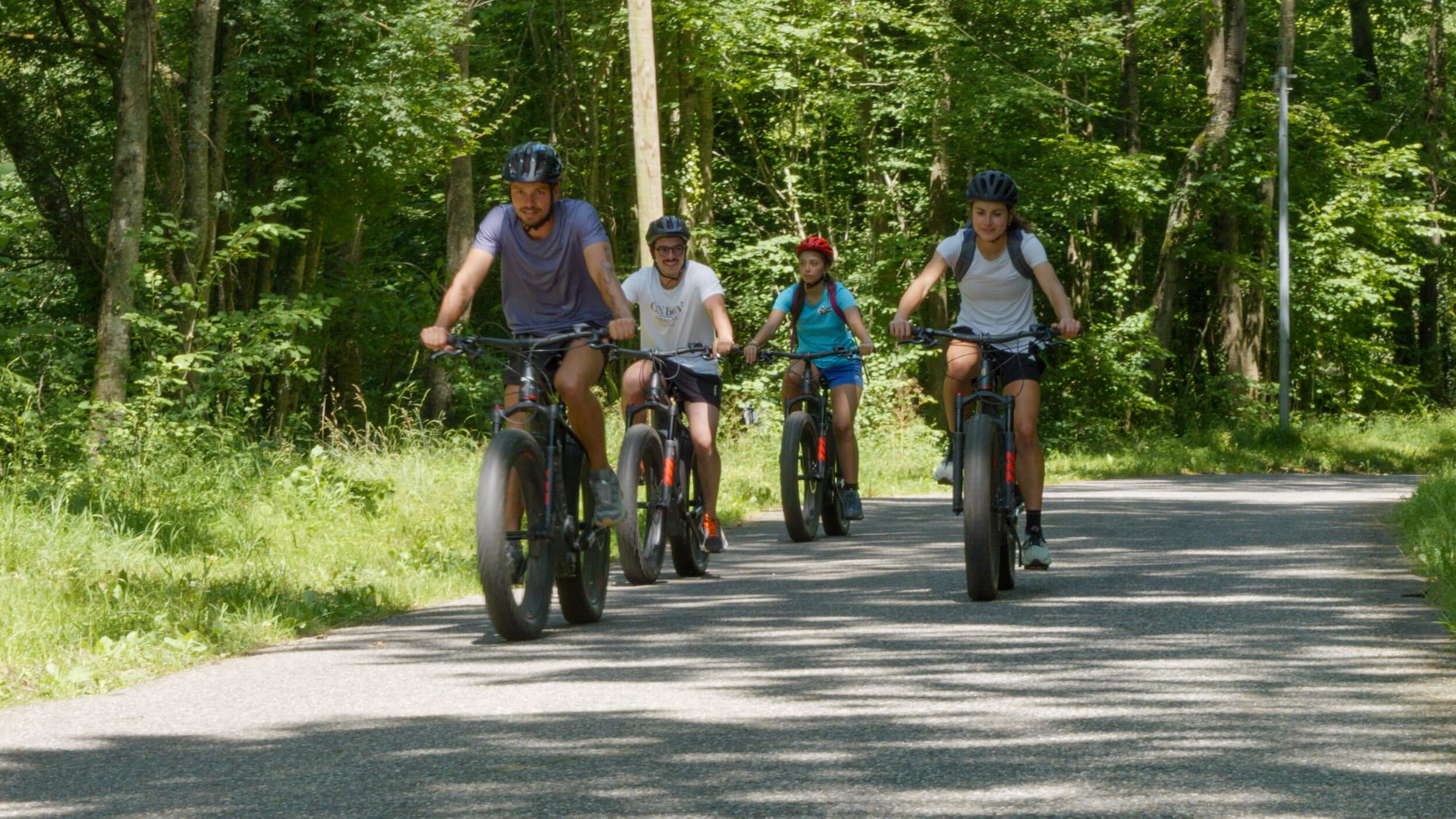 Quatre personnes font du vélo électrique sur un chemin forestier en été 