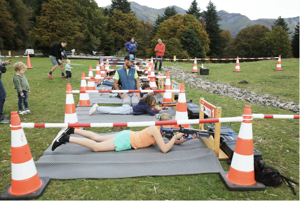Groupe de personnes pratiquant le tir à la carabine sur une plateforme en plein air, avec des cônes de signalisation orange et blanc pour délimiter la zone.