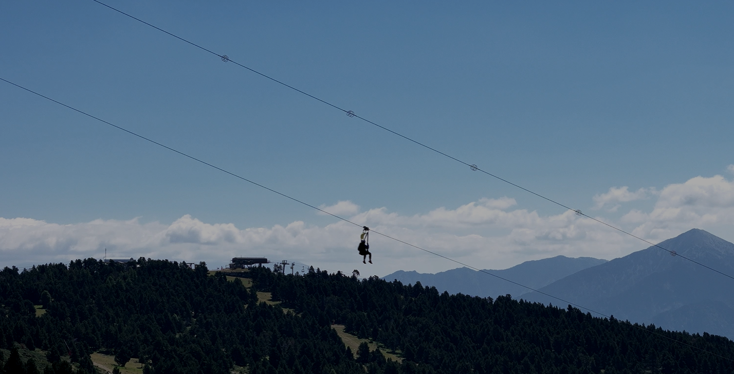Personne faisant de la tyrolienne au-dessus d'une forêt en montagne avec un ciel bleu et des nuages.