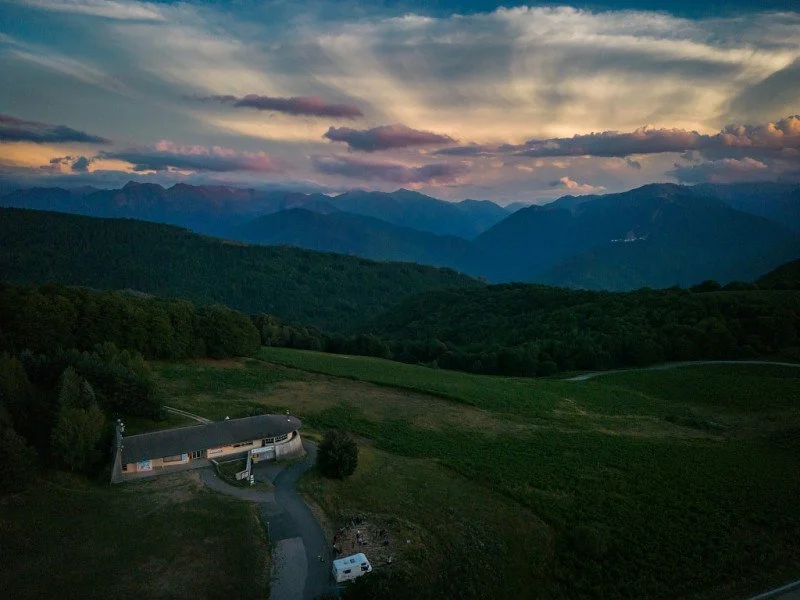 Paysage de montagnes au crépuscule avec un ciel coloré, vue sur des collines verdoyantes et une maison avec une allée