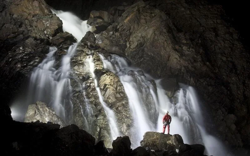 Personne debout près d'une cascade souterraine dans une grotte rocheuse.