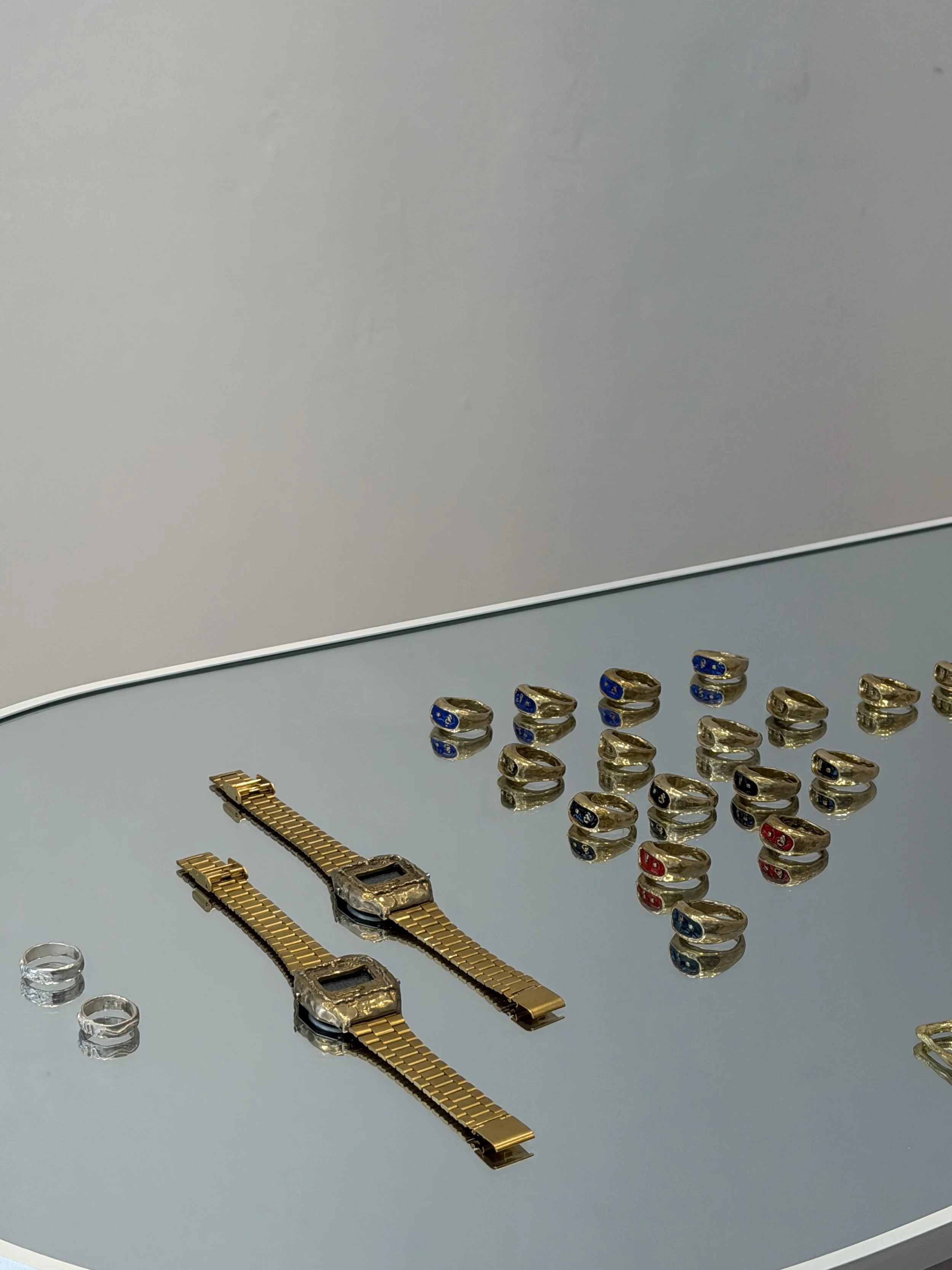Collection of gold and silver rings and watches on a reflective glass surface.