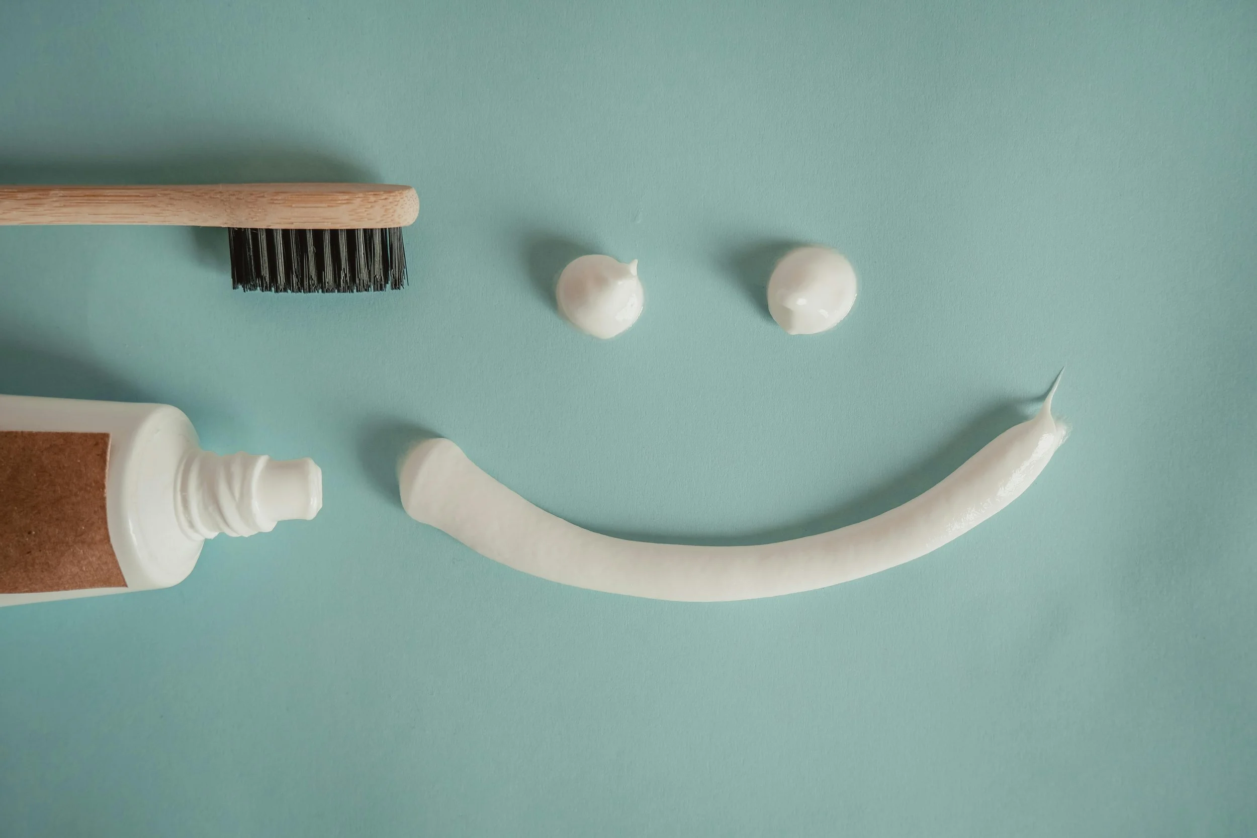 A toothbrush with white toothpaste and two dollops of white cream on a light blue background.