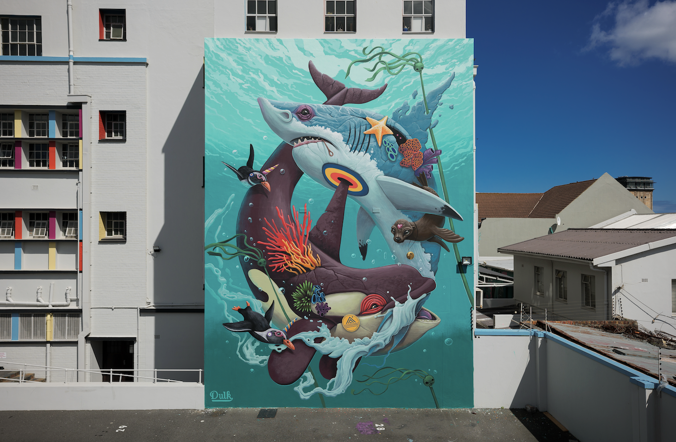 Colorful mural of an underwater scene featuring a large shark, a whale, seals, penguins, starfish, corals, and seaweed on the side of a building