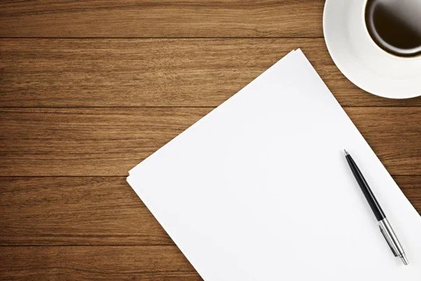 Empty sheet of paper on a wooden desk with a pen and a cup of coffee.