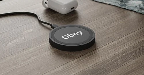 Wireless charging pad with the word 'Obey' on it, connected to a power source on a wooden surface.