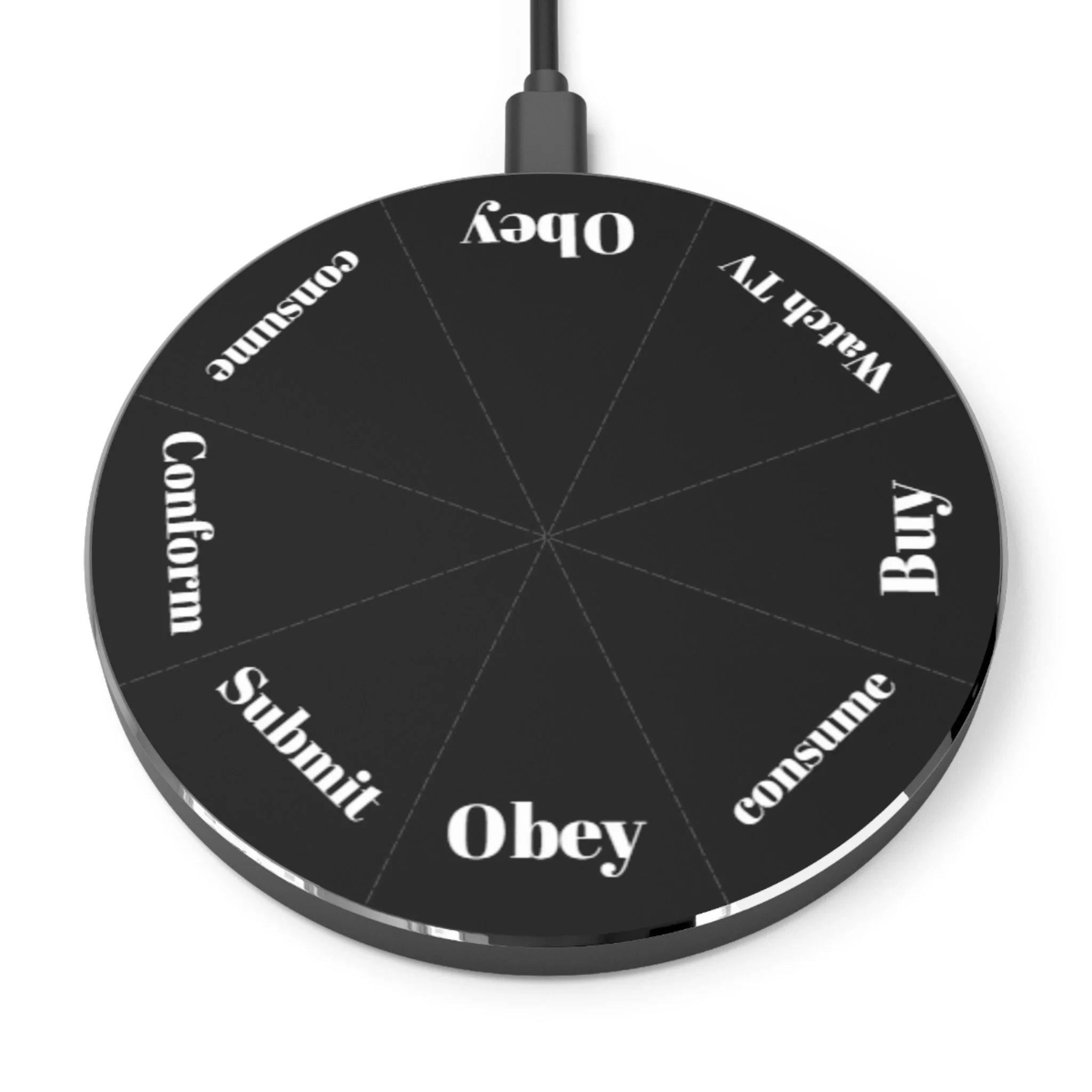 A black circular decision wheel with segments labeled with commands: obey, buy, consume, obey, submit, conform, consume, wallow, and ugly, with a black cord attached at the top.