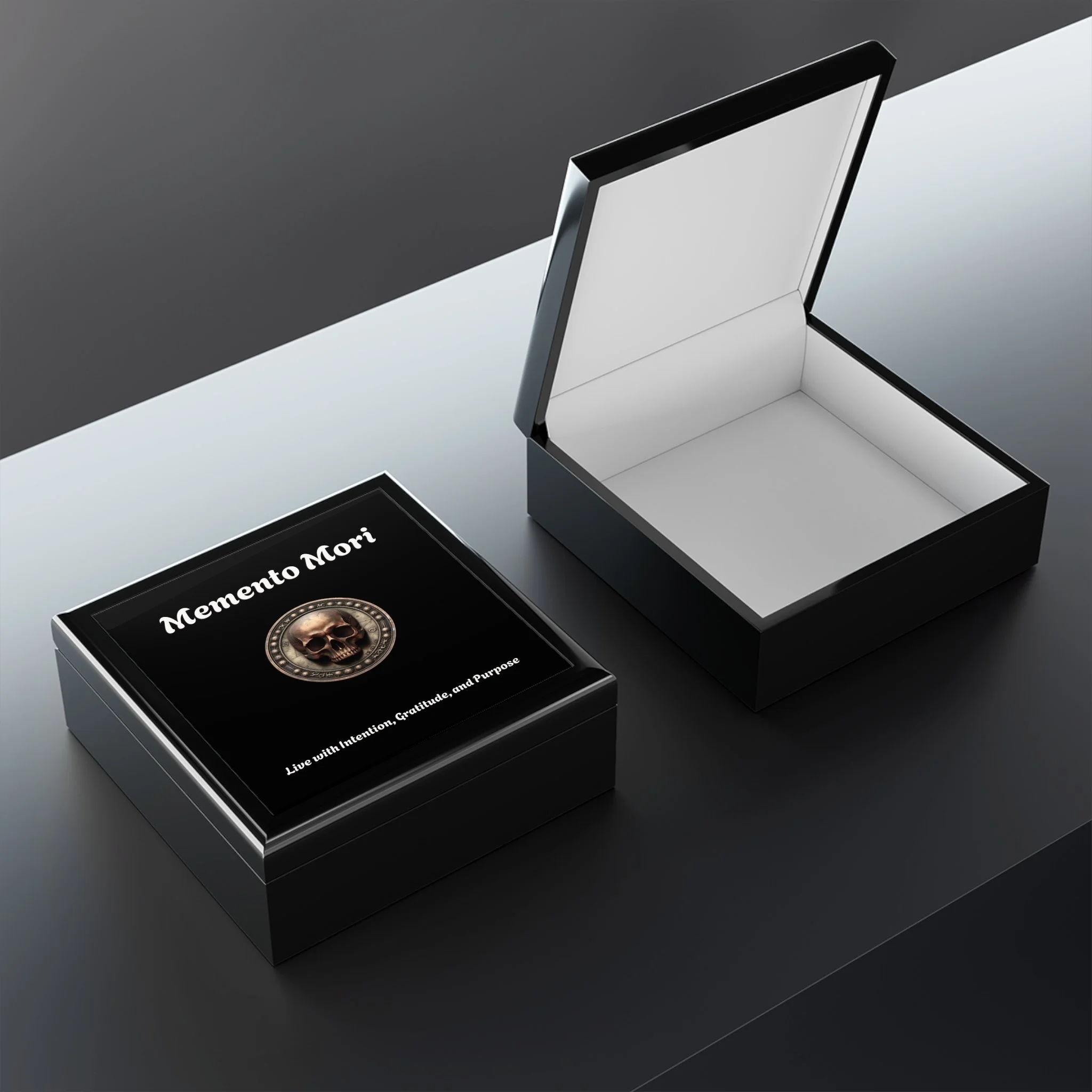 A black jewelry box with a skull emblem and the words 'Memento Mori', positioned next to an open empty jewelry box on a dark surface.