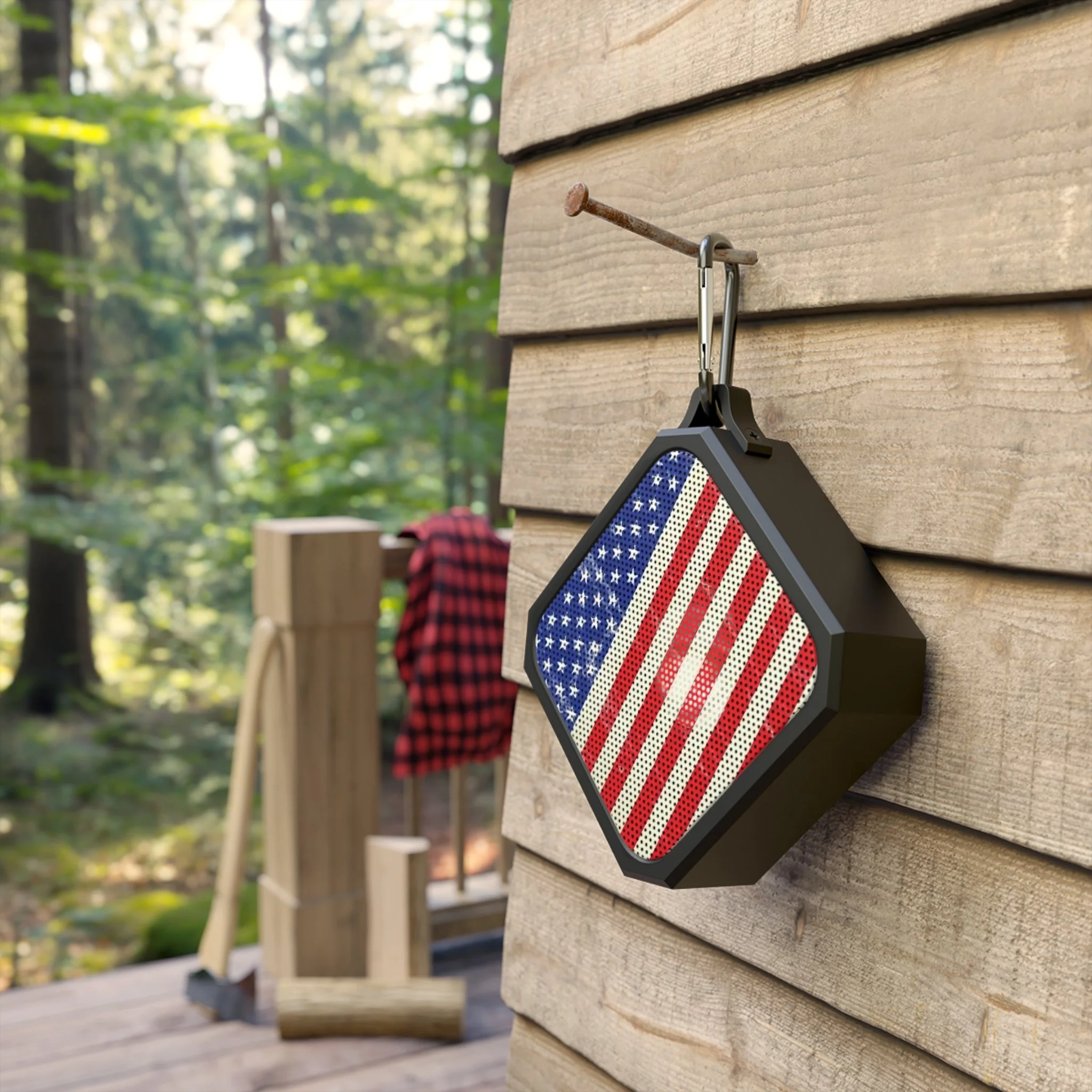 Bluetooth speaker with American flag design hanging from a nail on a wooden wall exterior of a house.