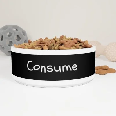 A white pet bowl with the word 'Consume' written on it, filled with dry dog food, with dog toys in the background.