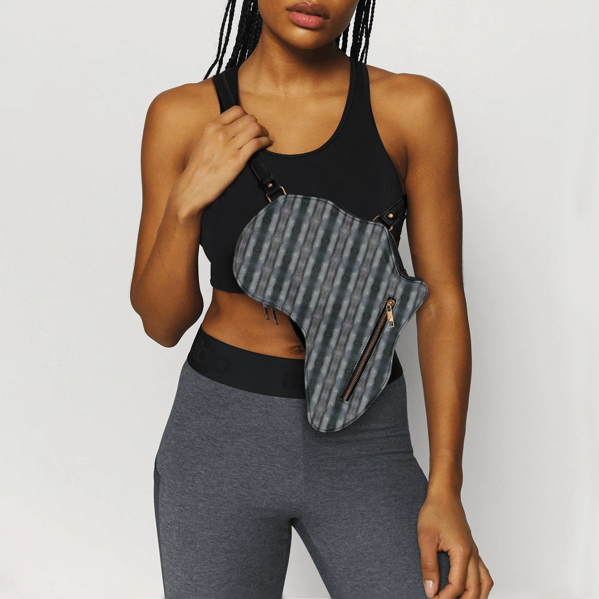 A woman in athletic wear with a black sports bra and gray leggings, holding a gray and black striped crossbody bag with a zipper pocket, against a plain white background.