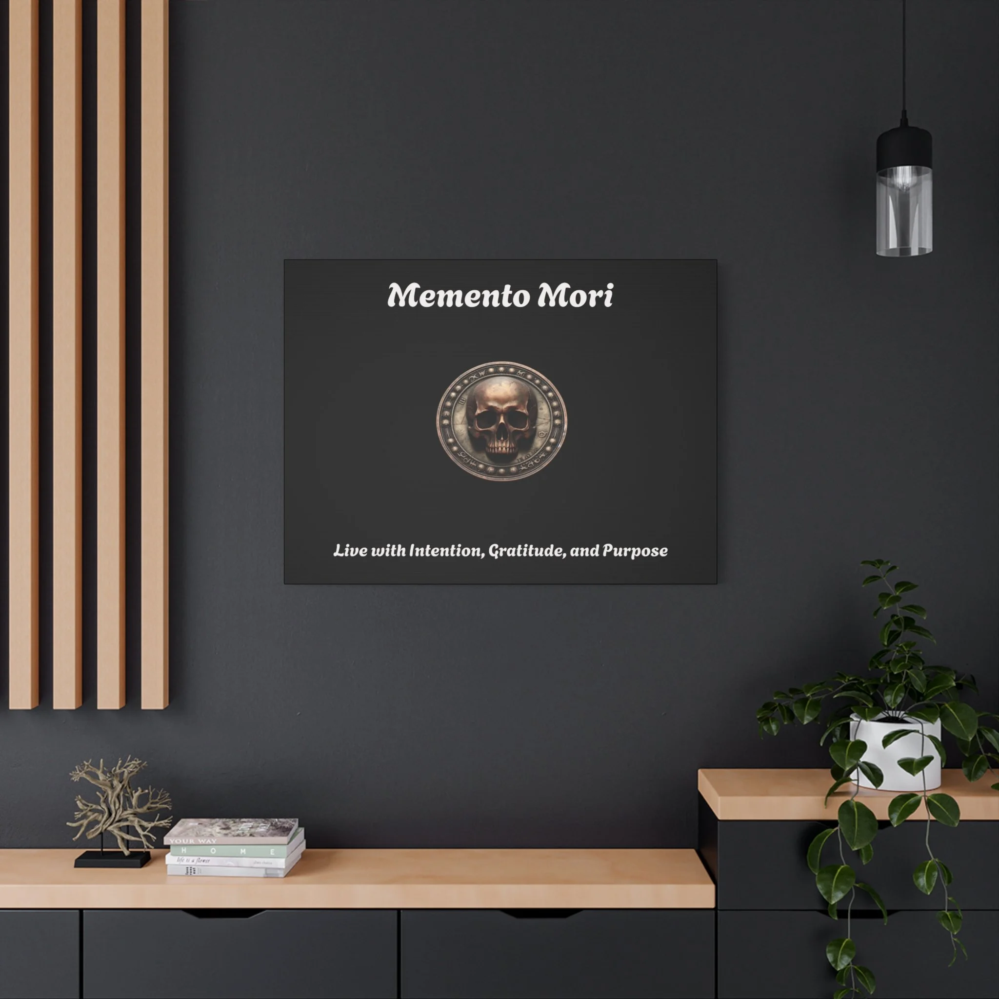 A dark gray wall with a framed art piece titled "Memento Mori" featuring a skull surrounded by a circular metallic design. Below, there is a quote that says "Live with Intention, Gratitude, and Purpose." To the right, a black pendant light hangs. On 