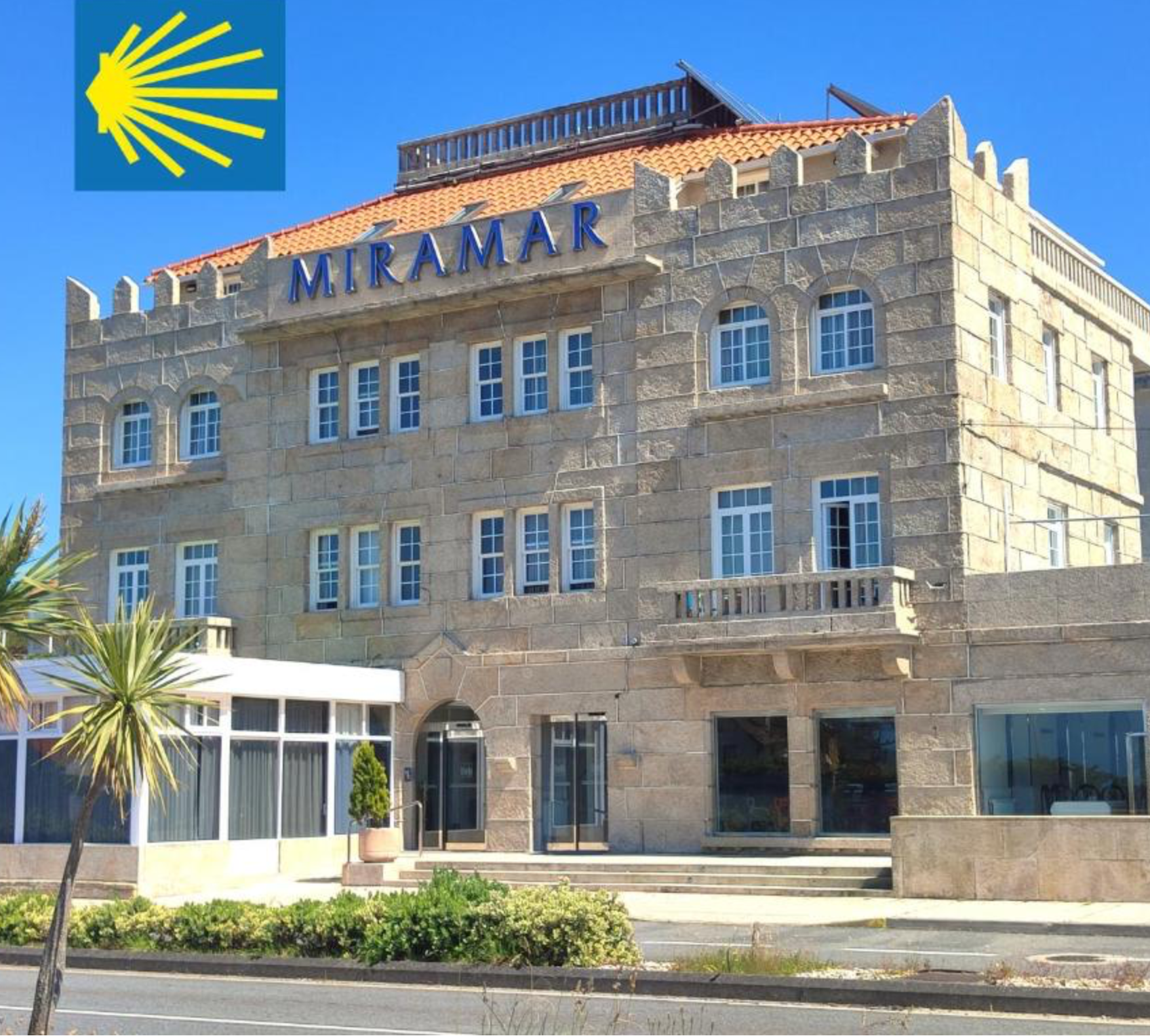 Edificio de piedra con el cartel ‘MIRAMAR’ en la fachada y un logo amarillo en la esquina superior izquierda, con una estructura de ventanas en diferentes niveles y una terraza en la azotea.
