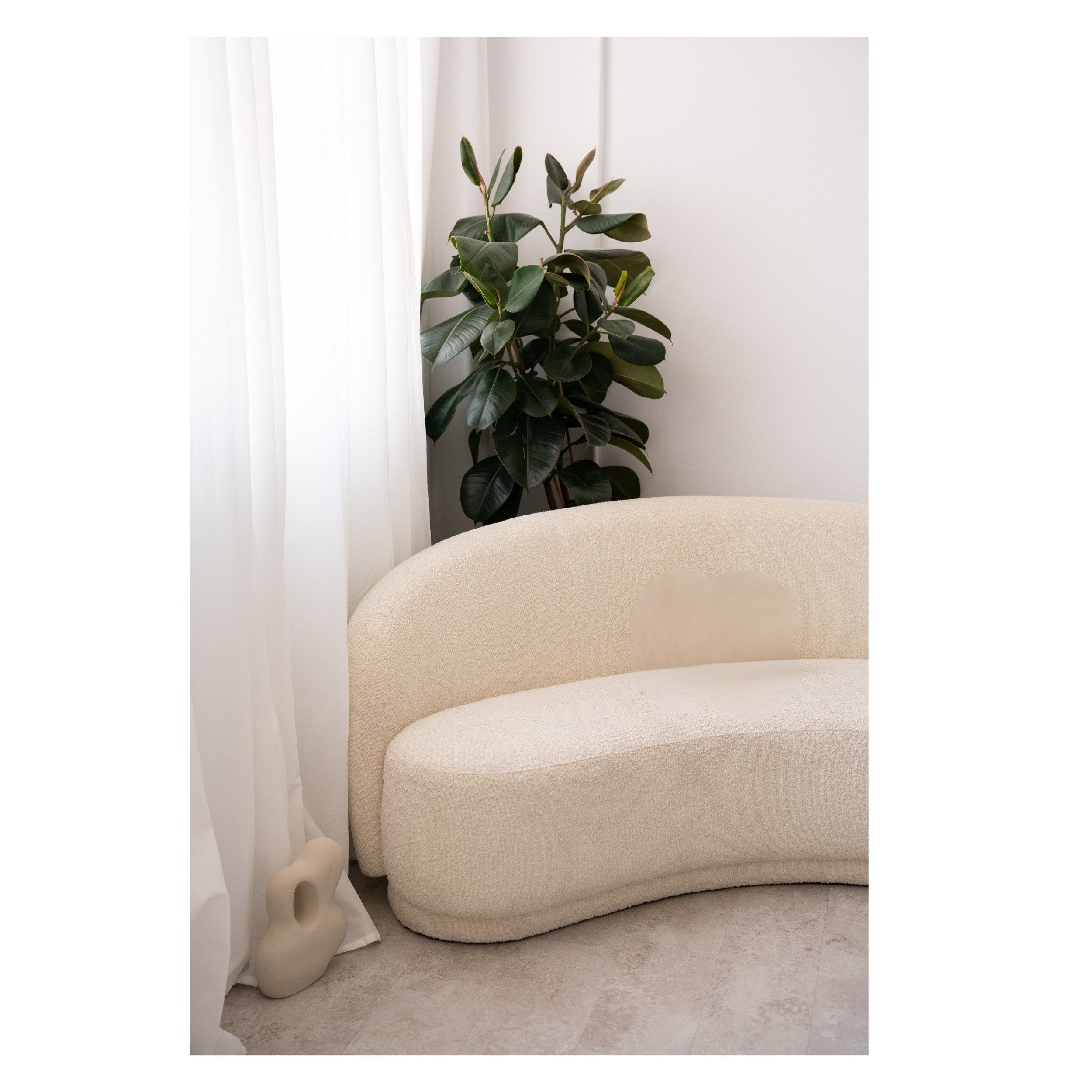 Interior scene with a large green houseplant near a white curtain and a beige upholstered chair.