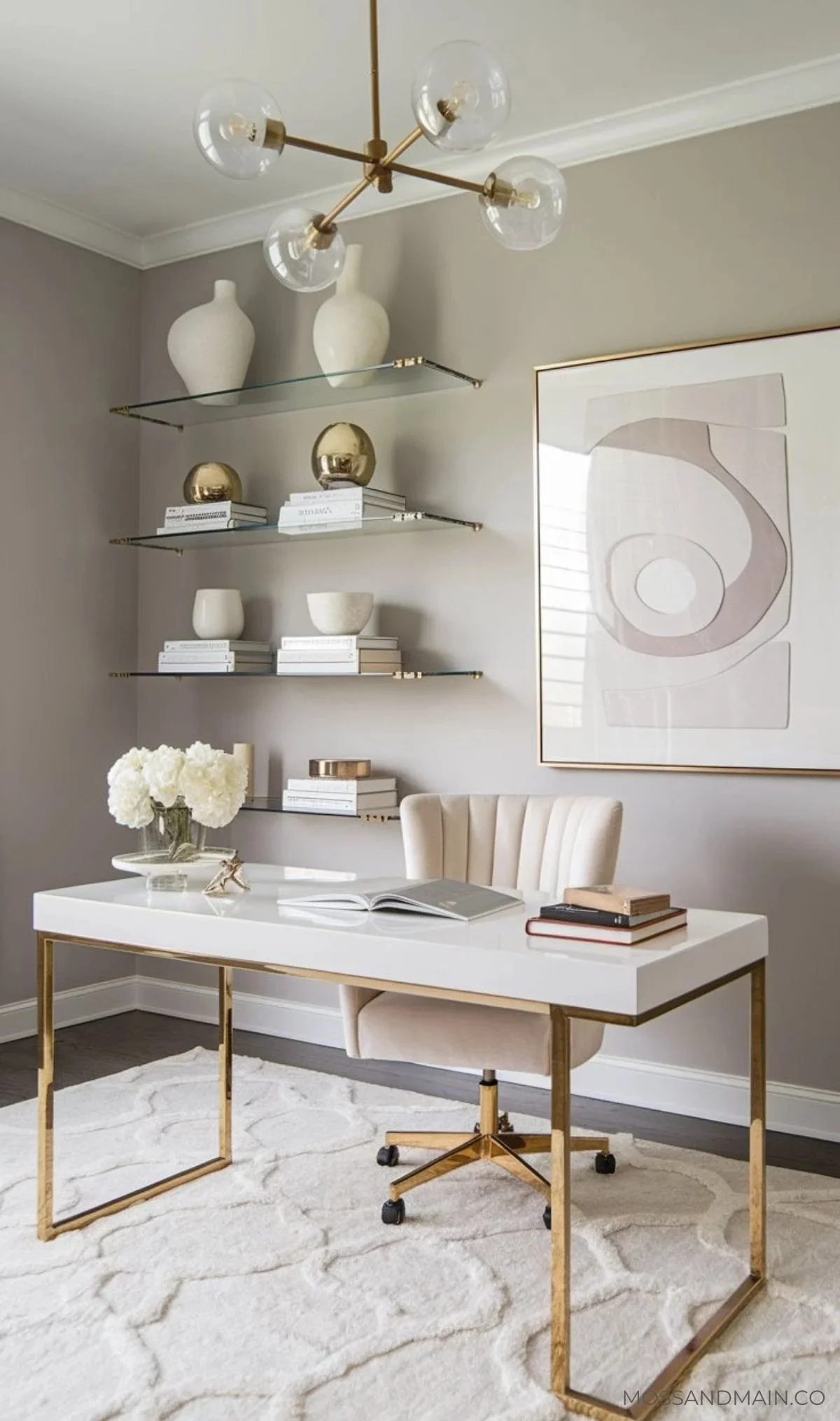 Modern home office with white desk, beige swivel chair with gold accents, abstract artwork, floating glass shelves with vases and decorations, chandelier with clear globes, and a white textured rug.