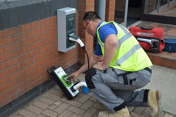 Technician charging an electric vehicle at an electric vehicle charging station outdoors.