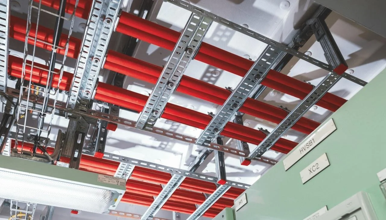 Ceiling with red pipes and metal cable trays in an industrial or electrical setting.