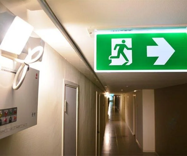 Green emergency exit sign with running figure and arrow pointing to the right in a hallway.