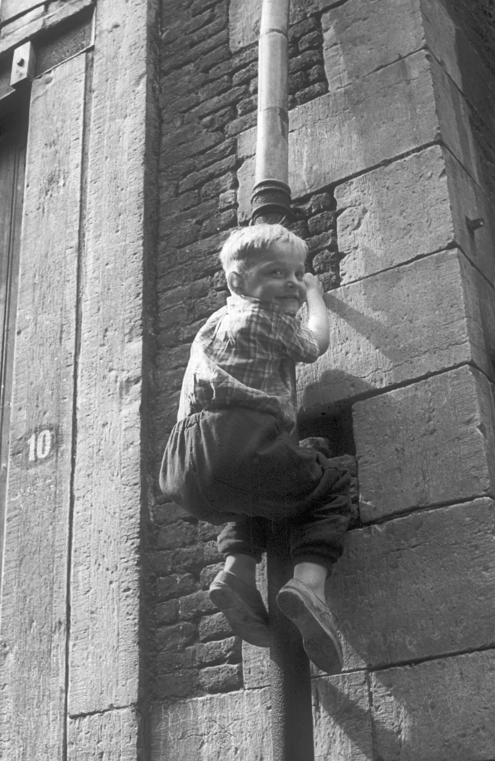 Kind in regenpijp in Stokstraatkwartier, ca 1955 [WS]