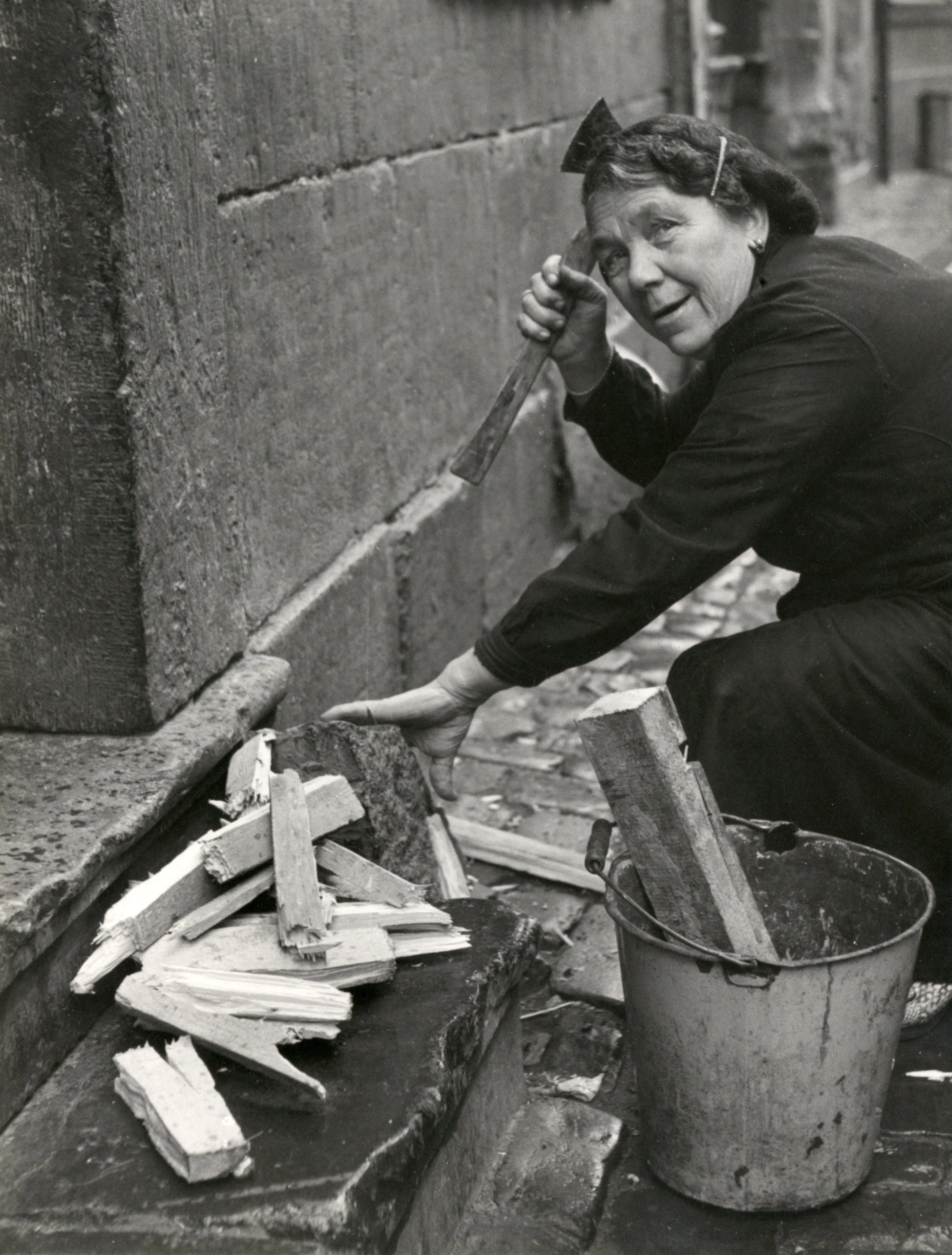 Vrouw in Stokstraat hakt houtjes, 1951 [NA]