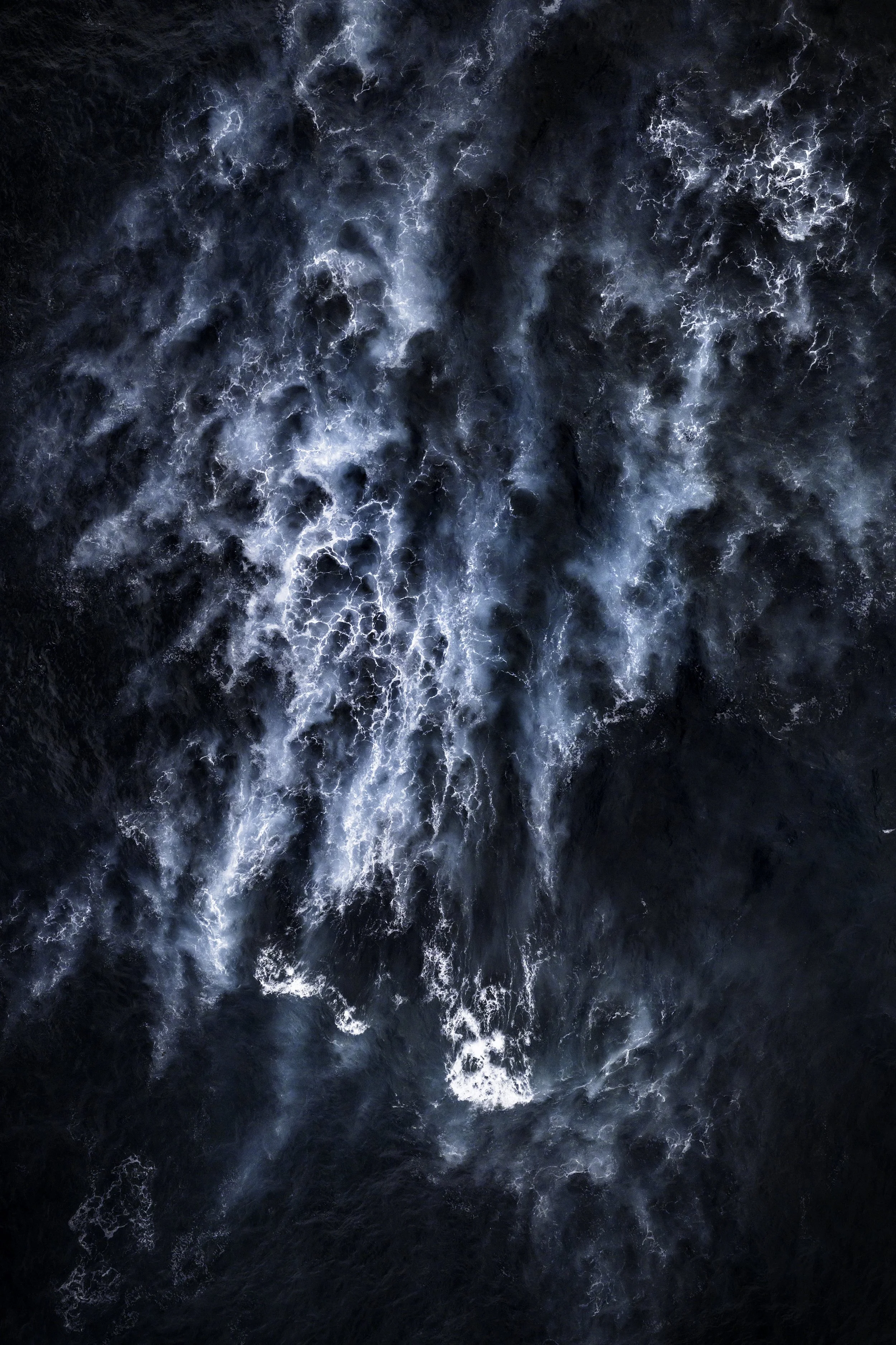 An aerial view of turbulent dark blue ocean water with white foam pattern.