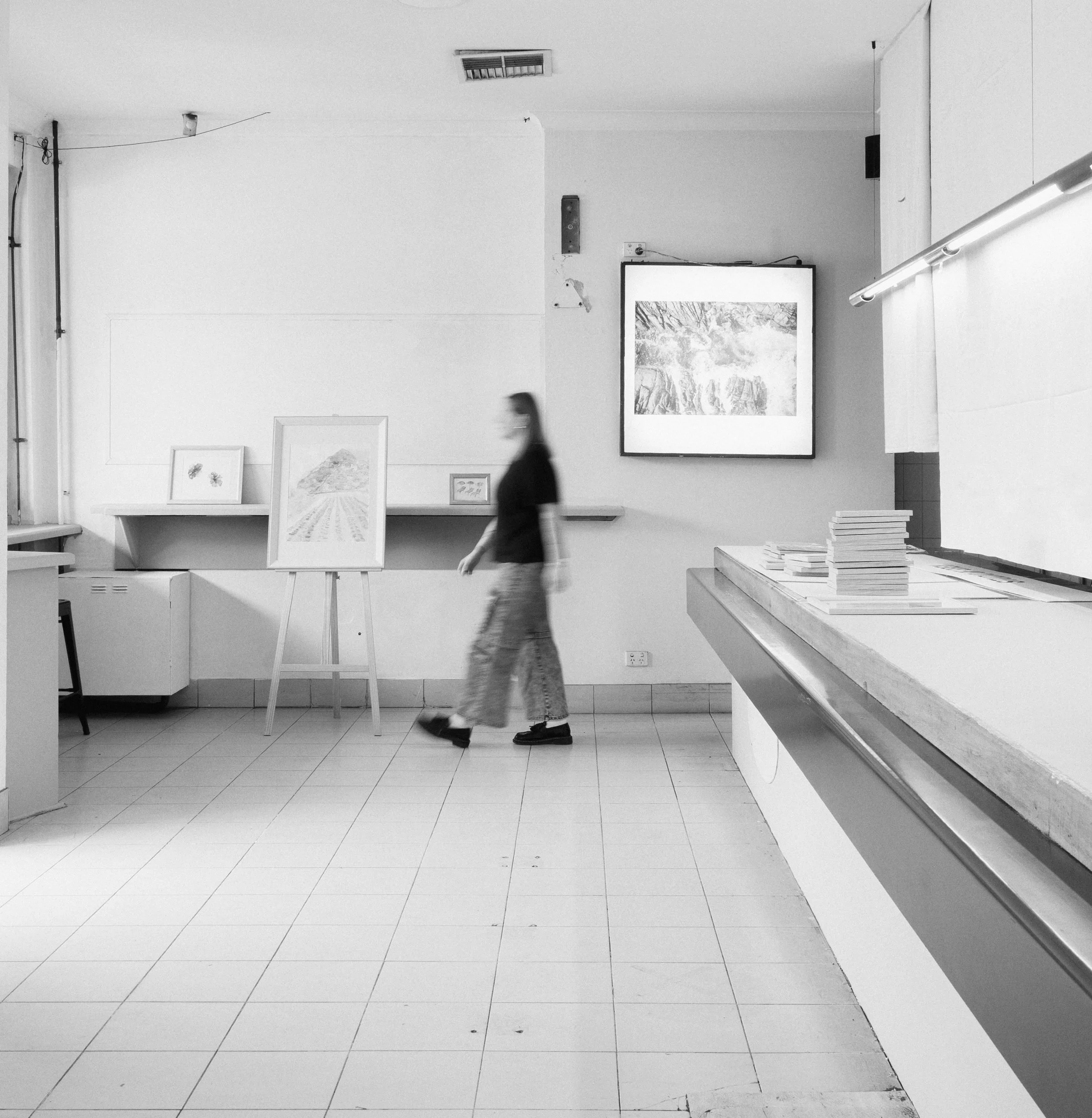 An art gallery with framed artwork on the walls and a person walking past.