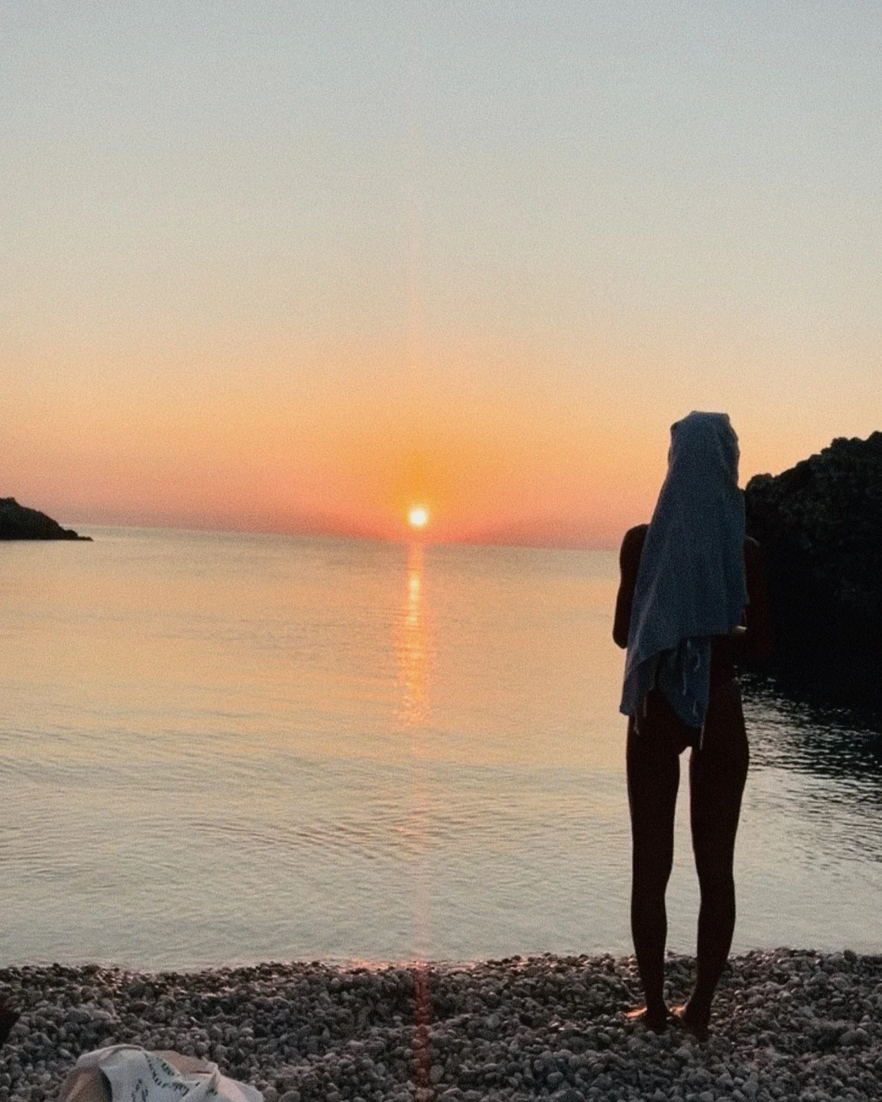 Person standing on rocky beach during sunrise, front view, overlooking calm ocean waters. Best moment of the day, raising with the day, sunrise, silence, peace, bliss.