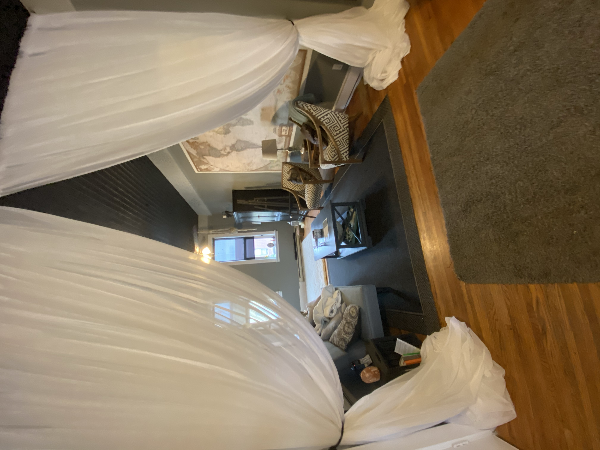 Living room with two chairs, a coffee table, a gray sofa with pillows, a map on the wall, a window with blinds, and a curtain, with hardwood floors.