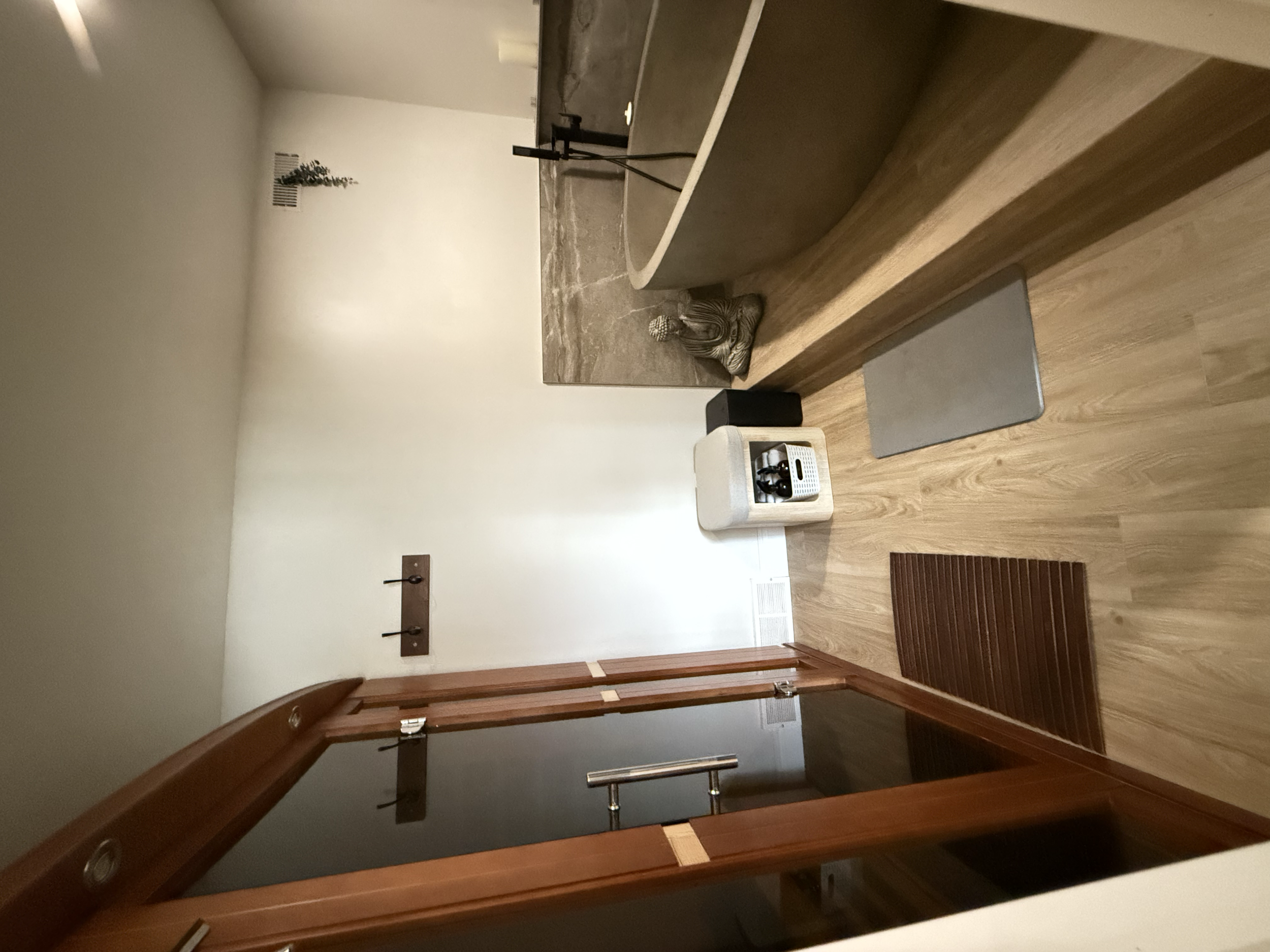 A small shrine with a Buddha statue, a gray mat, and a heart-shaped mirror on the wall next to the door.