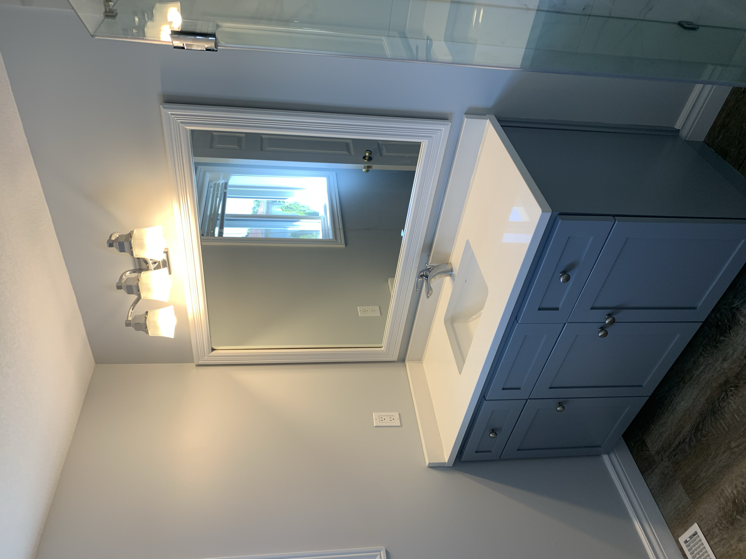 Bathroom vanity with sink, mirror, and light fixture, next to a window with a view outside.