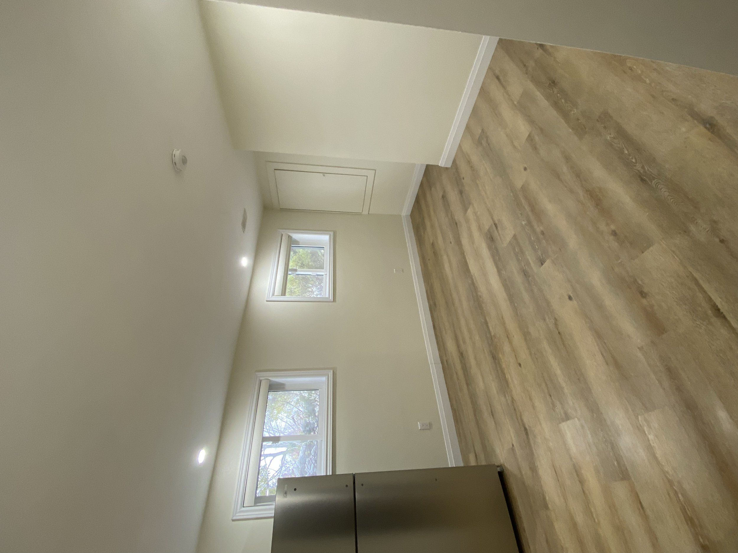 Empty room with white walls, two windows, hardwood flooring, and a white door.