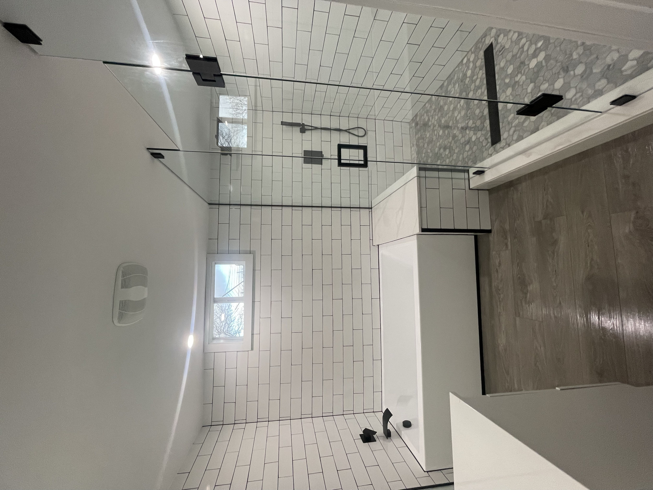Modern bathroom with white subway tile walls, a glass shower enclosure, a white vanity with a black trim, and wood-look flooring.