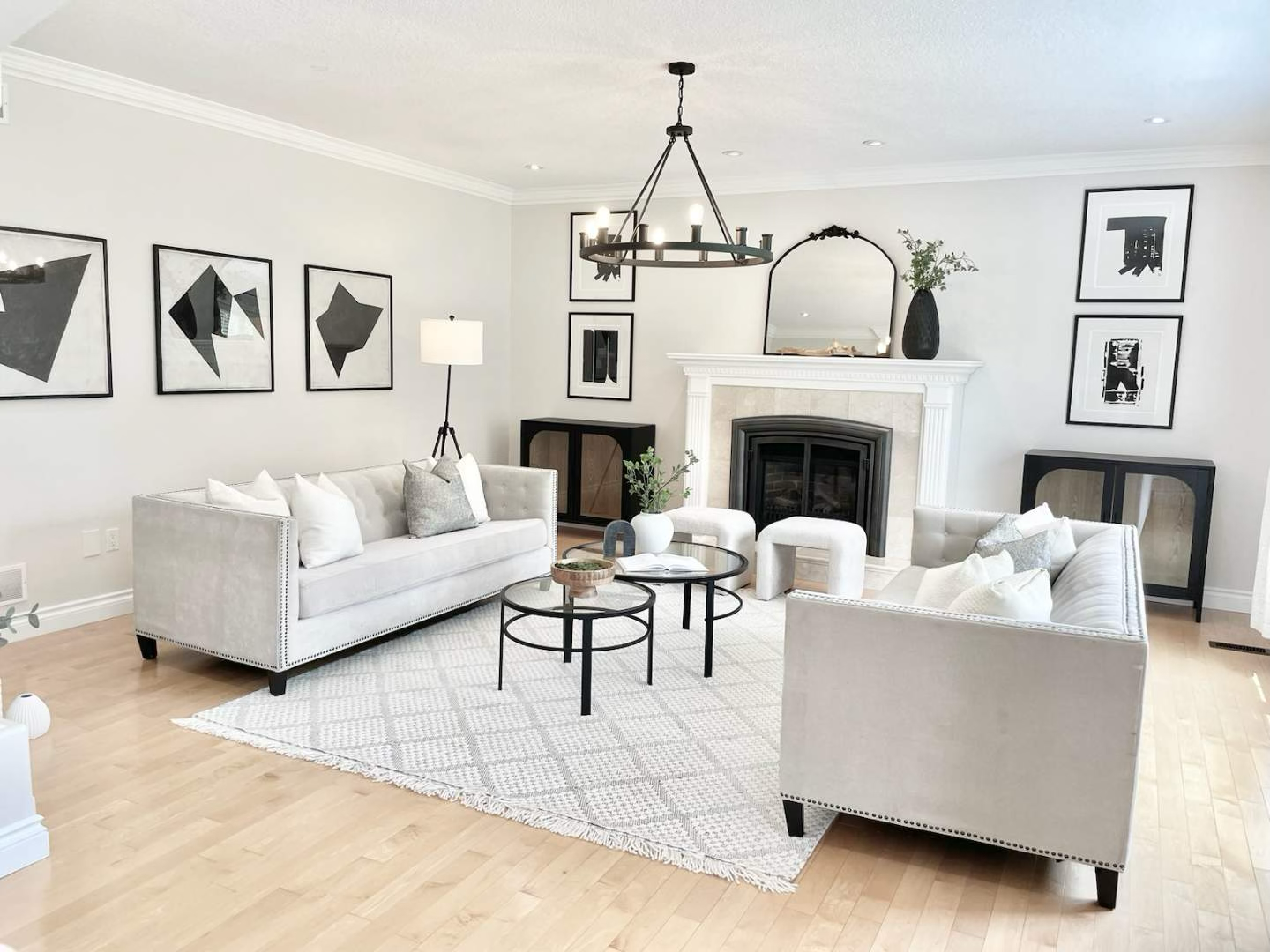 Modern living room with white sofas, a fireplace, black and white artwork, a chandelier, and decorative vases.