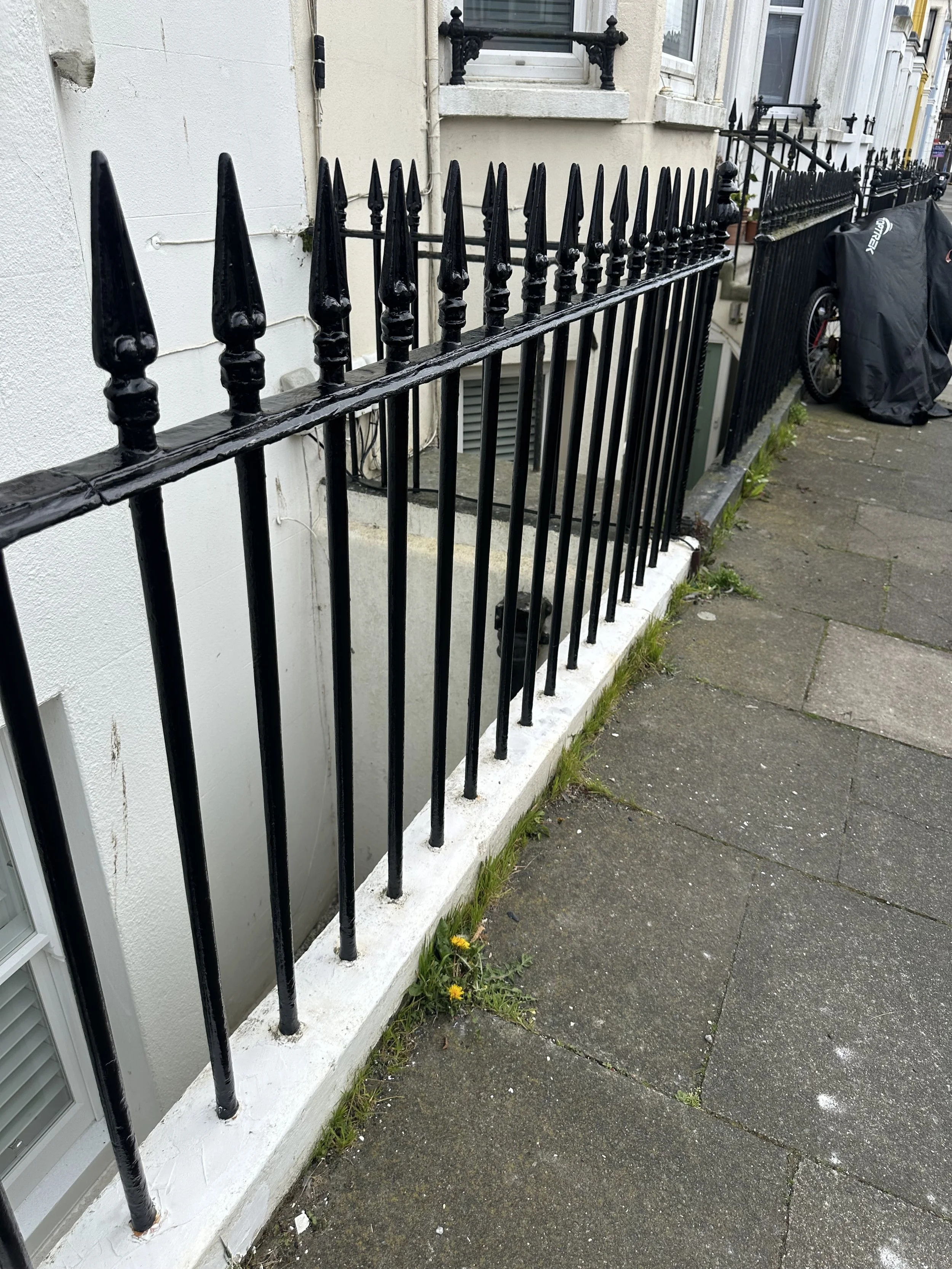 Black wrought-iron railings painted in Hammertite black metal paint, following rust removal, wire brushing and extensive sanding. The white masonry base wasn't part of the works. 