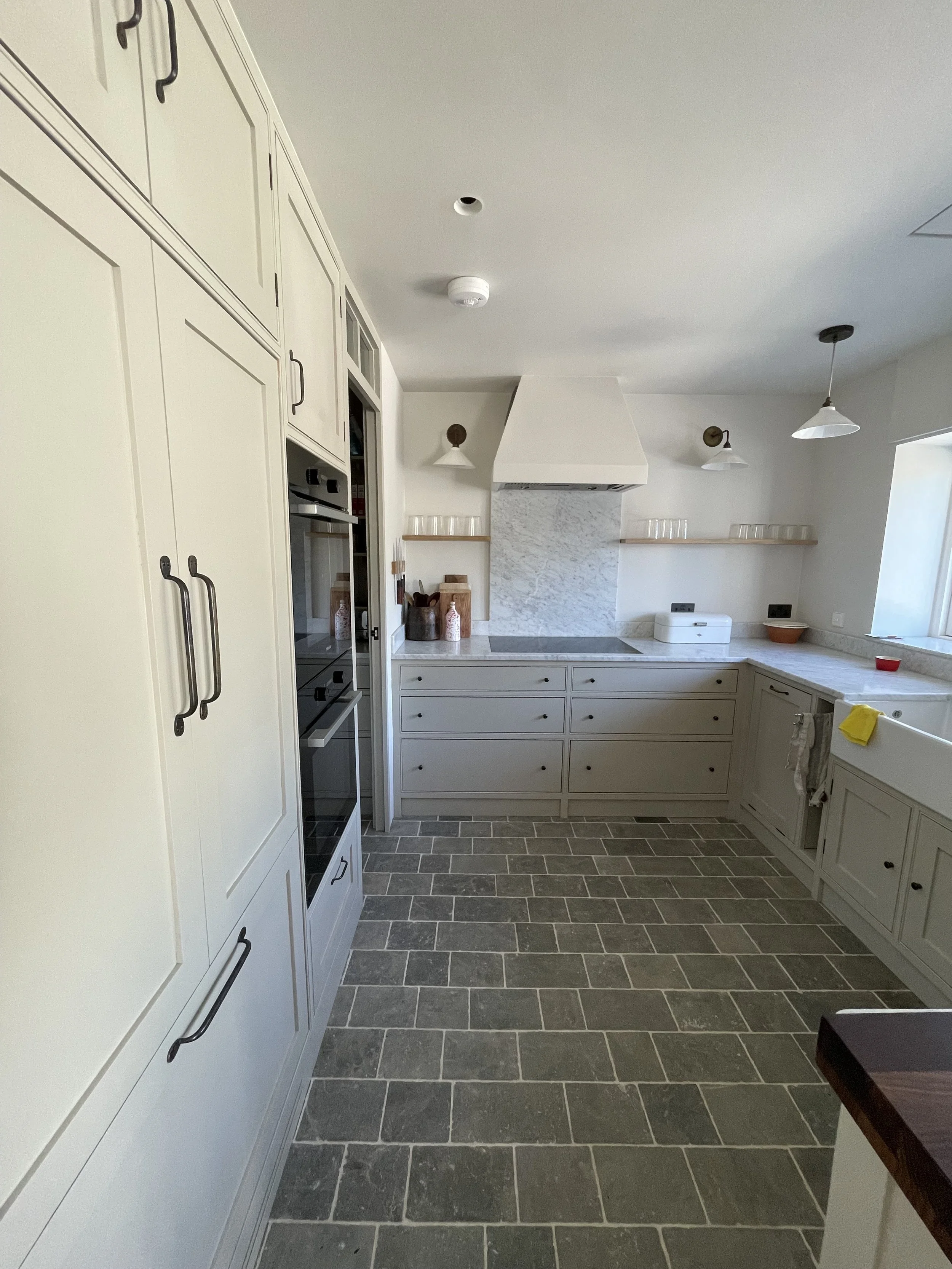 Kitchen with white cabinetry, gray tiled floor, marble backsplash, open shelves, and a window on the right side.