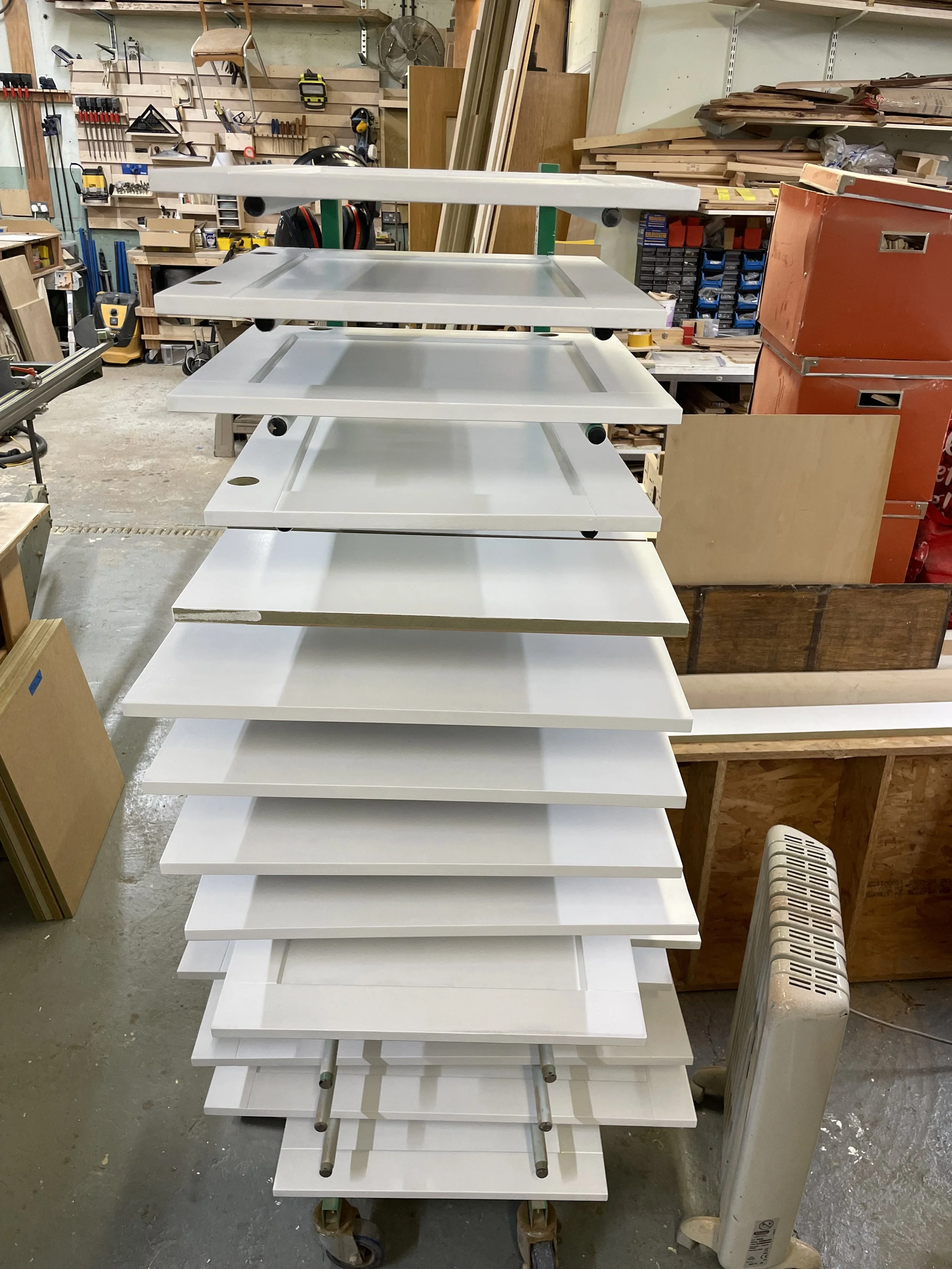 Cupboard doors and cabinet panels are painted in Sanderson white eggshell, and are drying on a rack in the workshop where the cabinetry was made