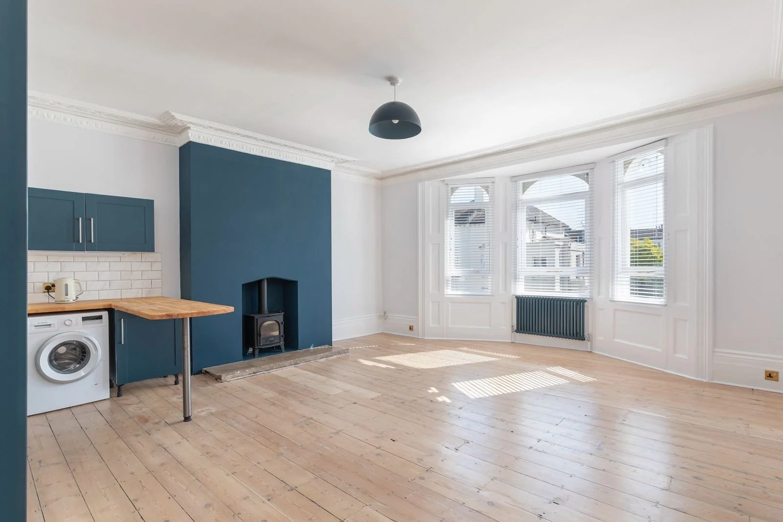 Finished refurbishment of a large kitchen/lounge (Dulux 'Rock Salt' Walls), with a large bay window. Chimney stack wall painted in 'Hague Blue' Matt by Farrow and Ball. Cabinetry in kitchen and radiator are Hague Blue (eggshell), bay windows are bril