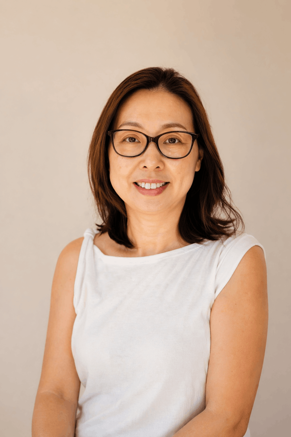 Portrait of a woman with shoulder-length brown hair wearing glasses and a white sleeveless top, smiling at the camera.