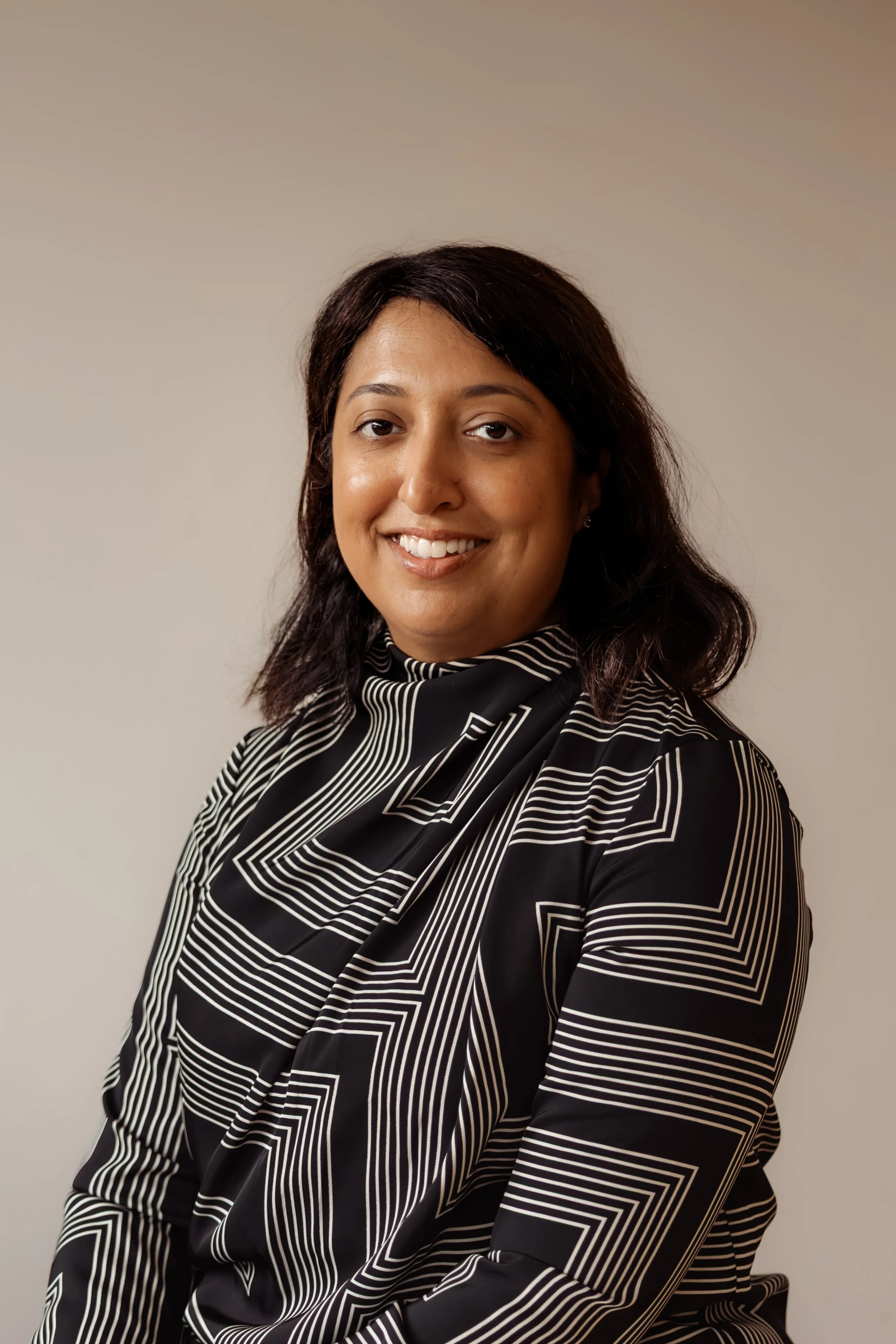 Portrait of a woman with dark hair wearing a black and white striped blouse, smiling against a neutral background.