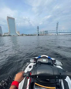 View from a boat on the water with a city skyline featuring a tall building and a bridge in the background.